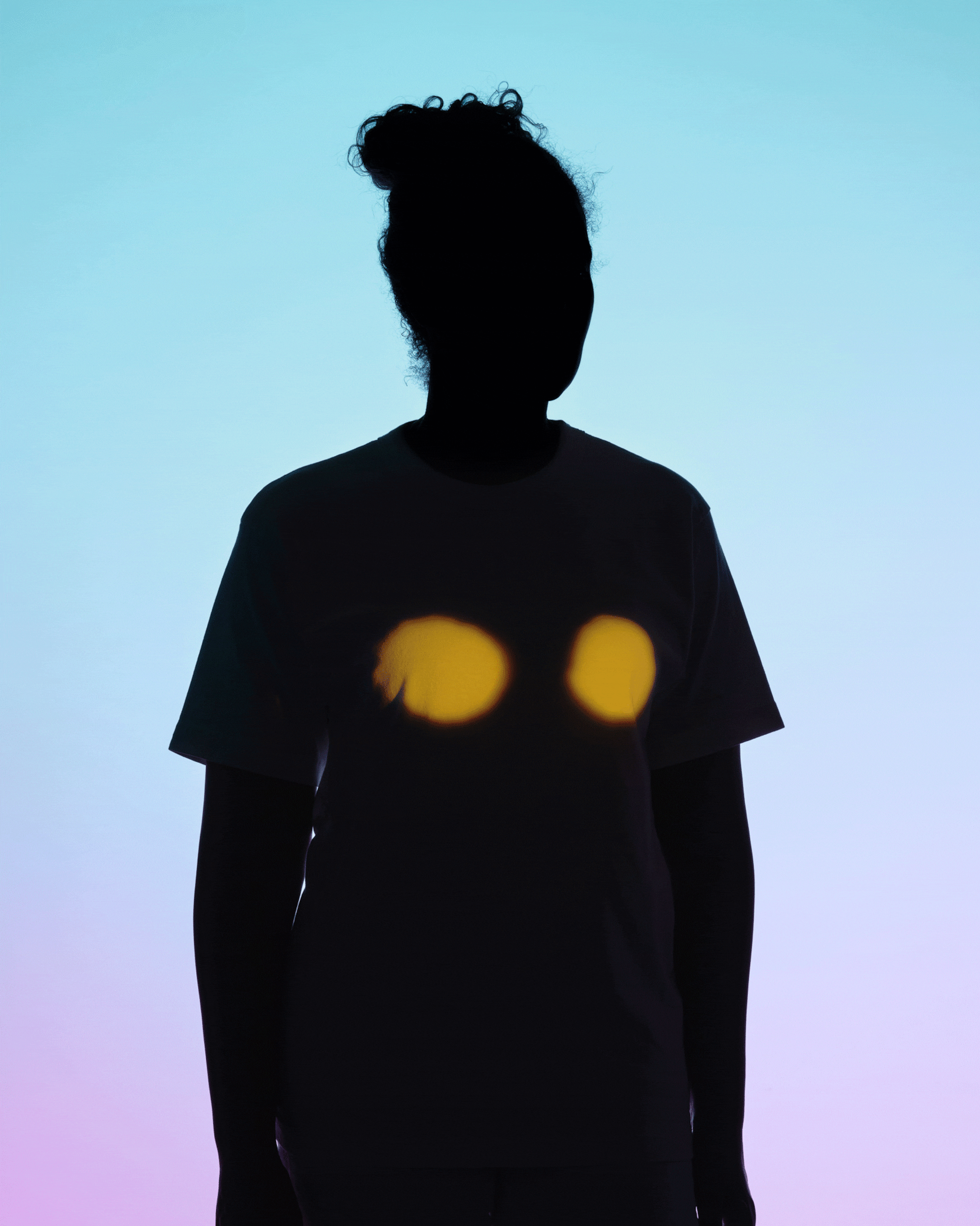 A woman silhouetted against a background that fade from light blue to light pink; projections of a heart, breasts, and ovaries cycle every second, appearing on the silhouetted woman's body