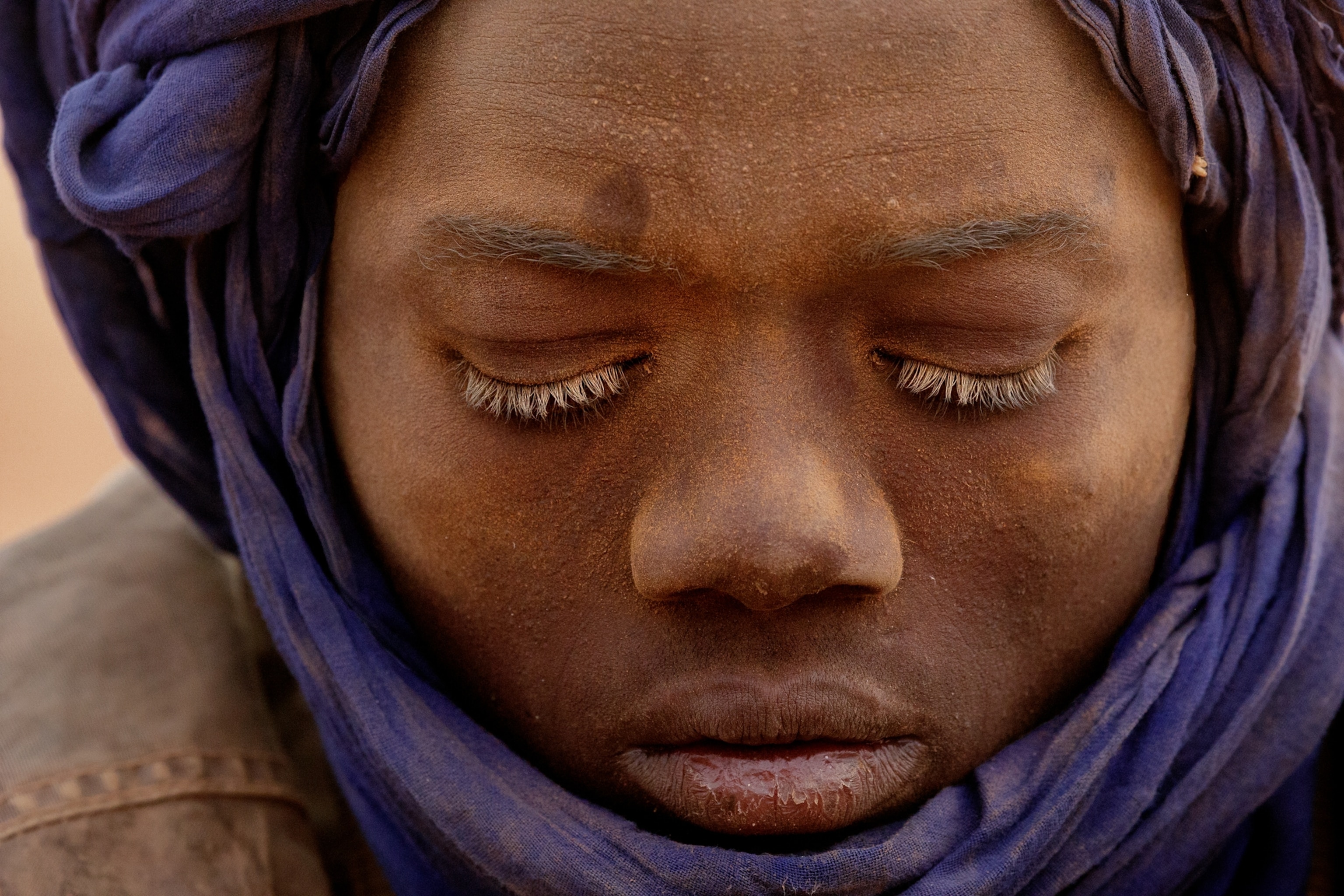 a young teen boy dusted with sand wearing a purple head scarf