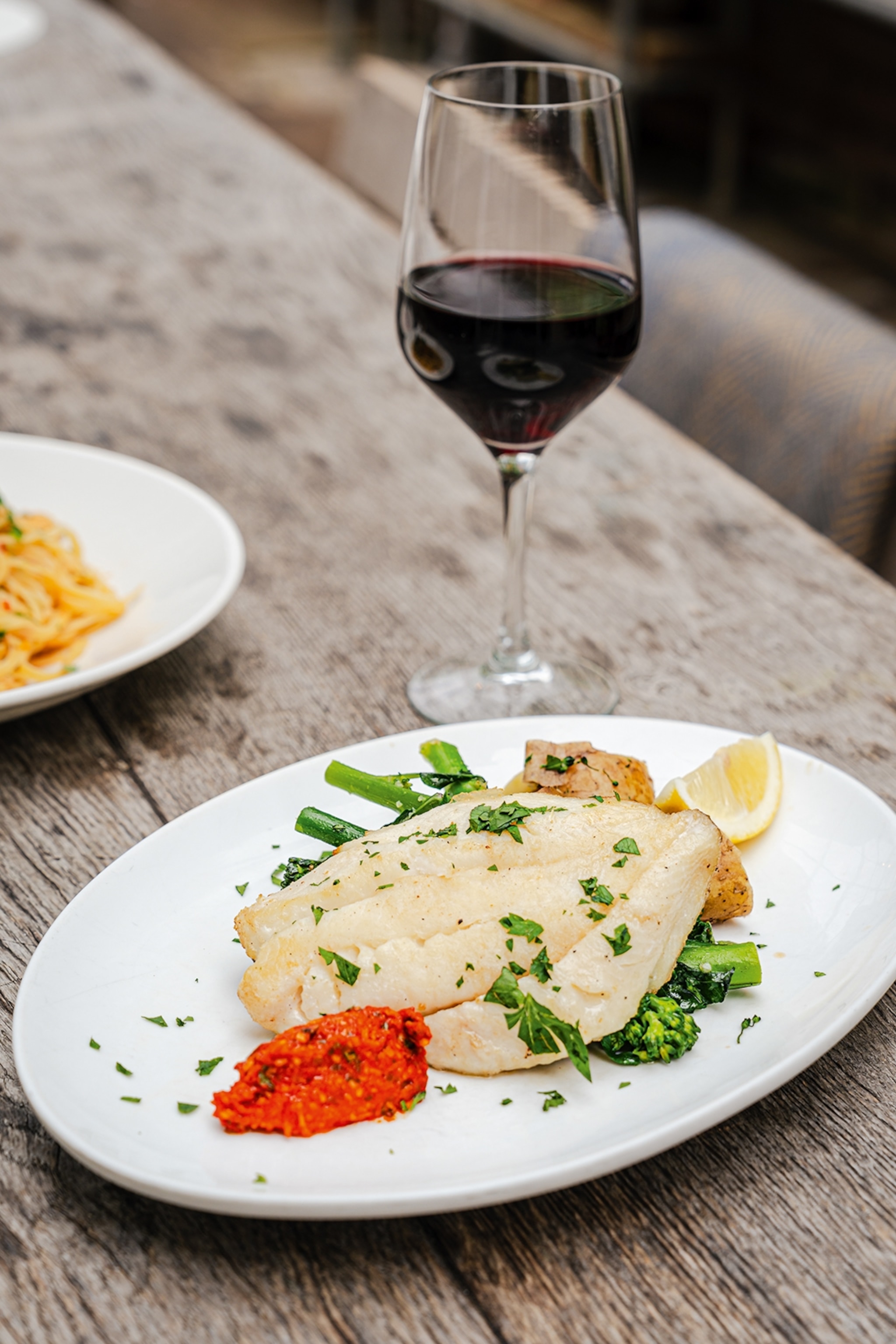 Fish placed on top of potatoes and broccoli next to a glass of wine