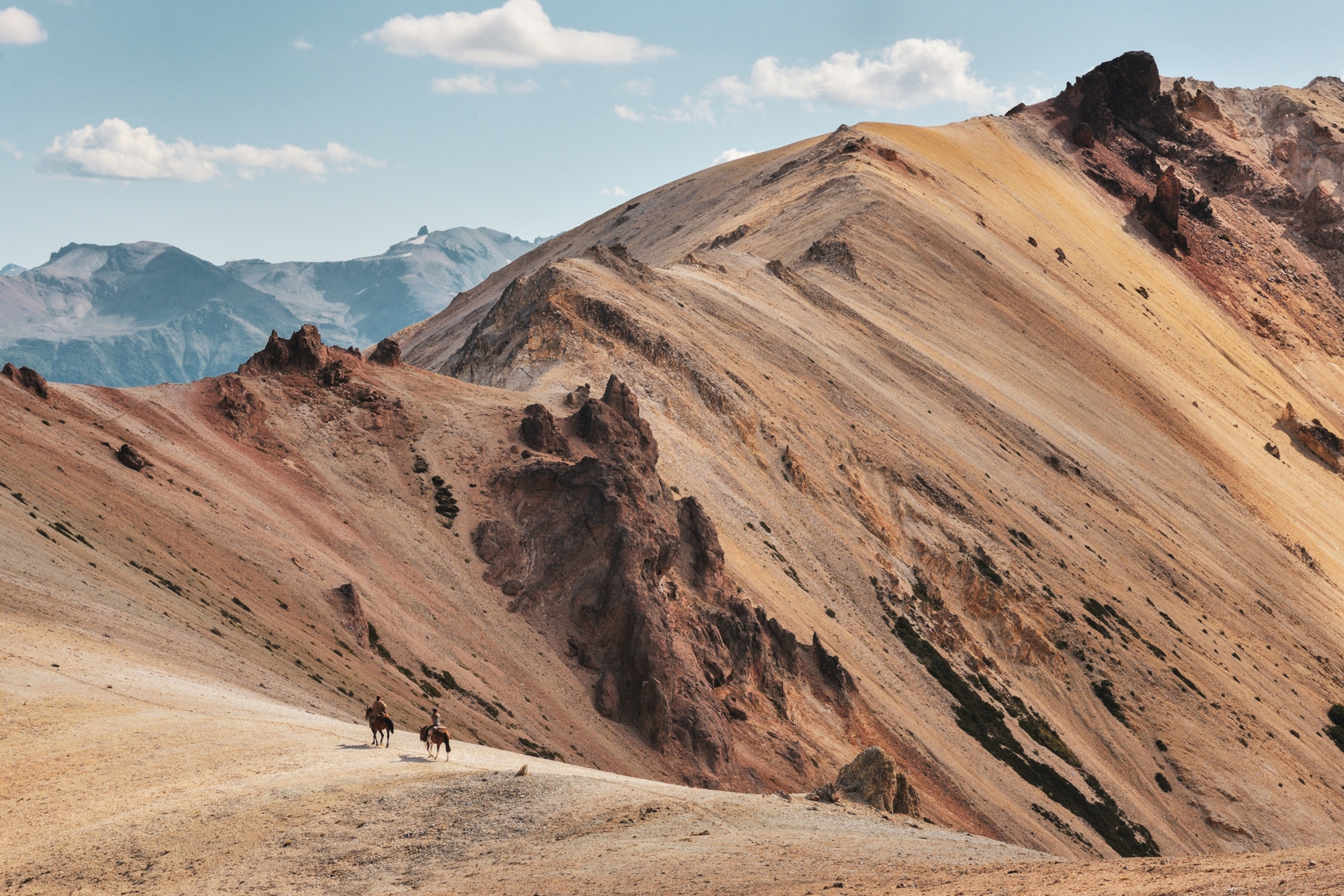 Sandy mountain tops with horse riders in the distance