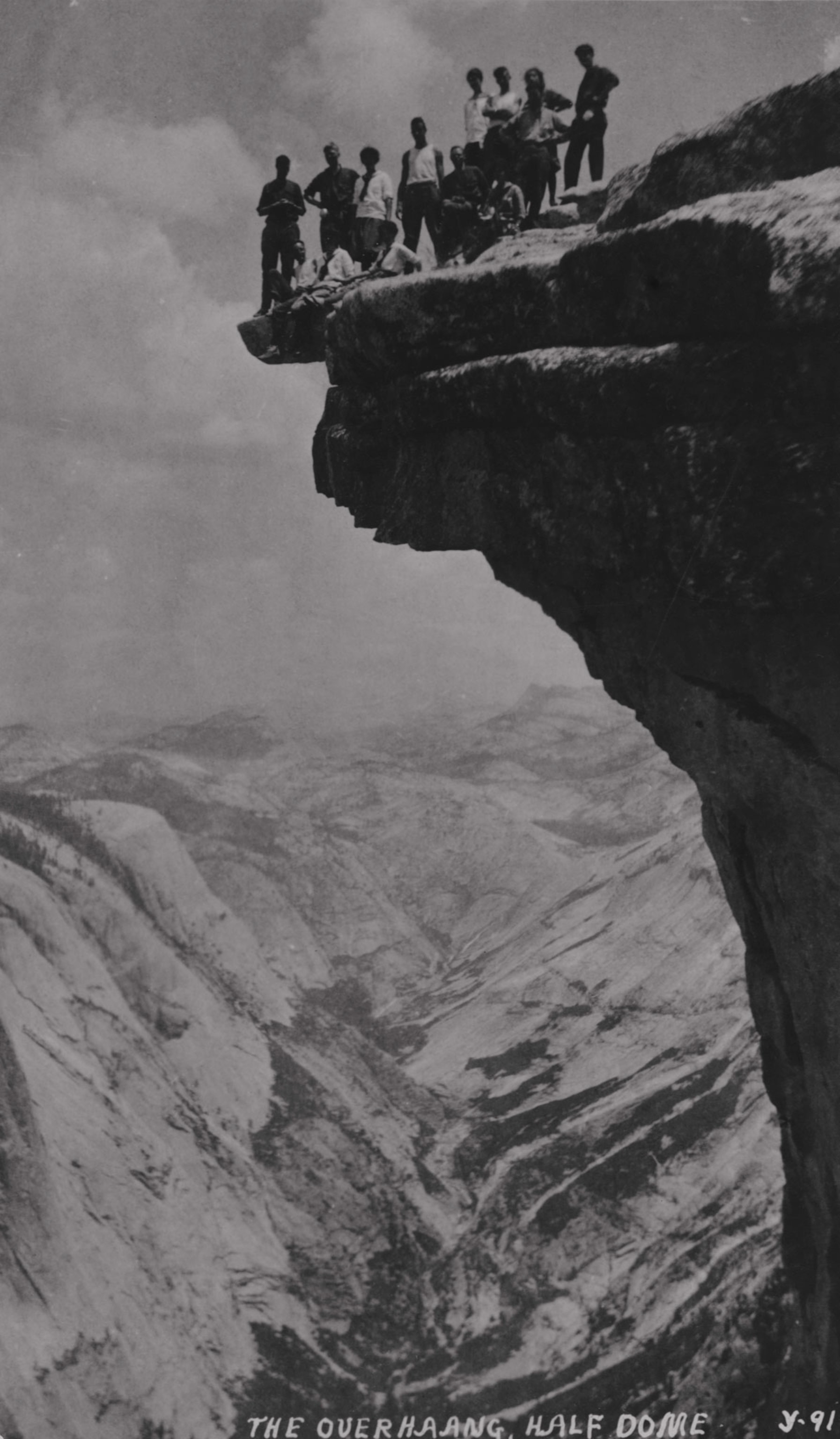 a group of people standing at the edge of Half Dome in 1919