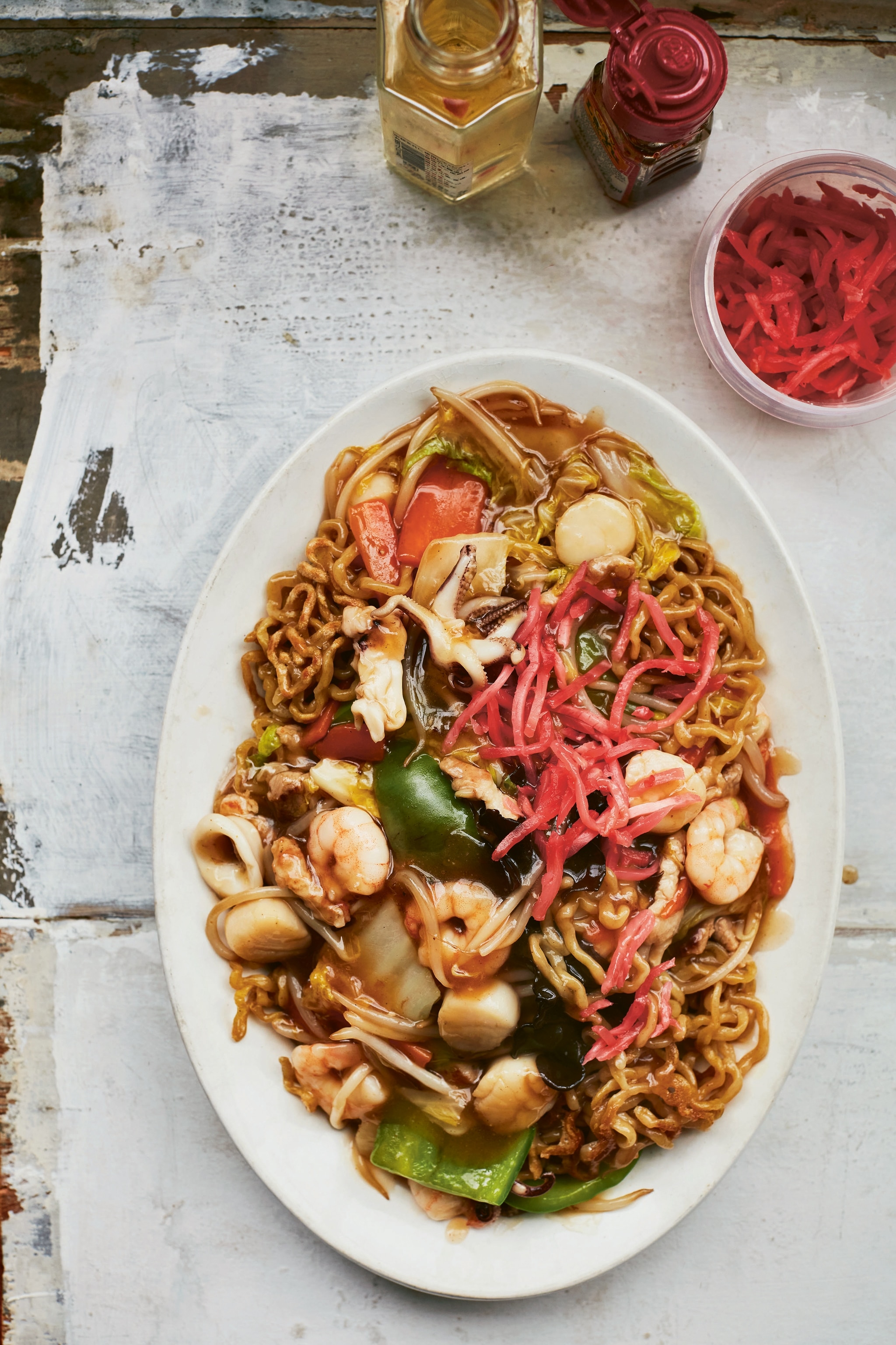 An oval plate of stir-fry noodles with pickled daikon, shrimp and vegetables.
