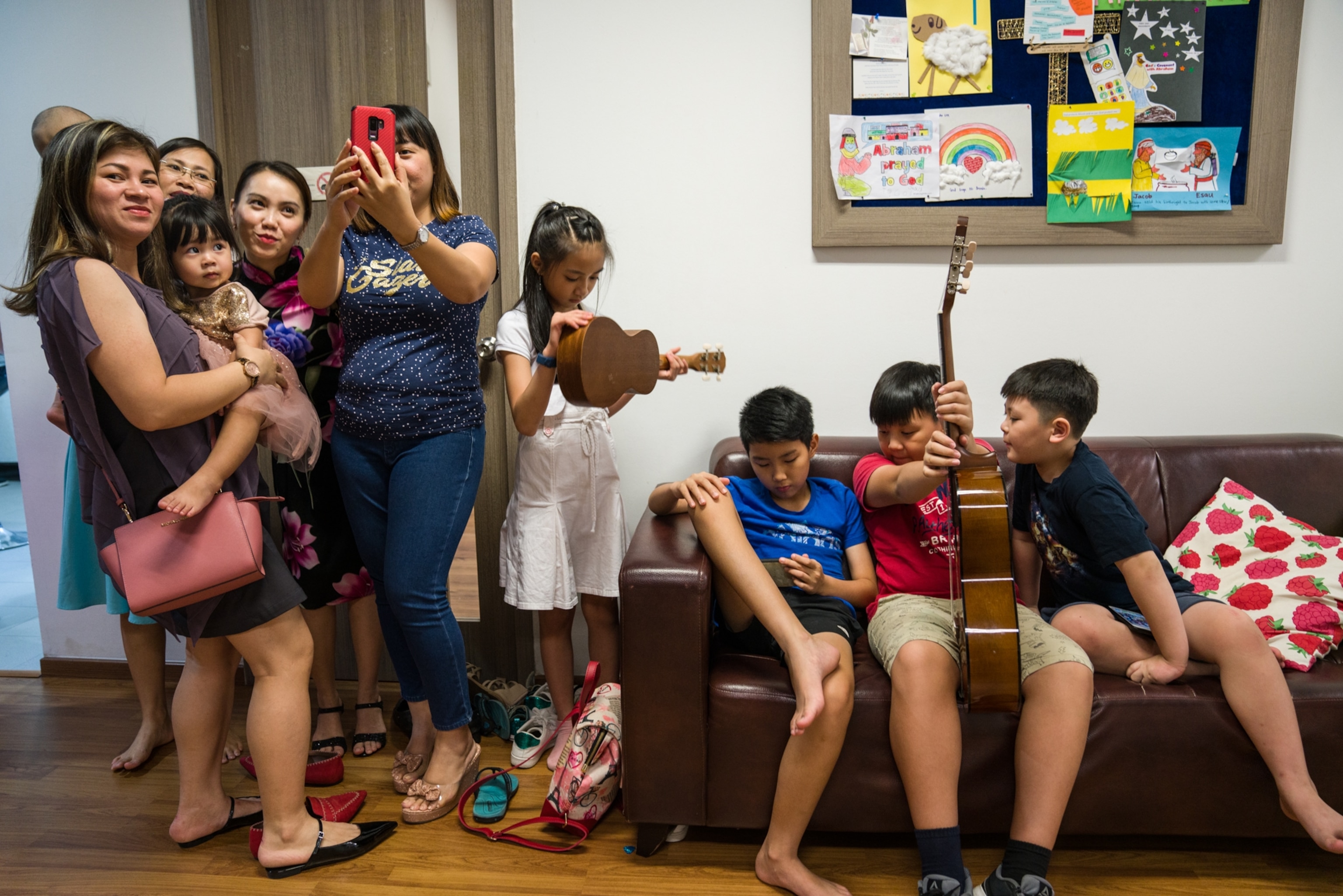 a group of children and mothers taking a selfie next to a couch with 3 more children on it
