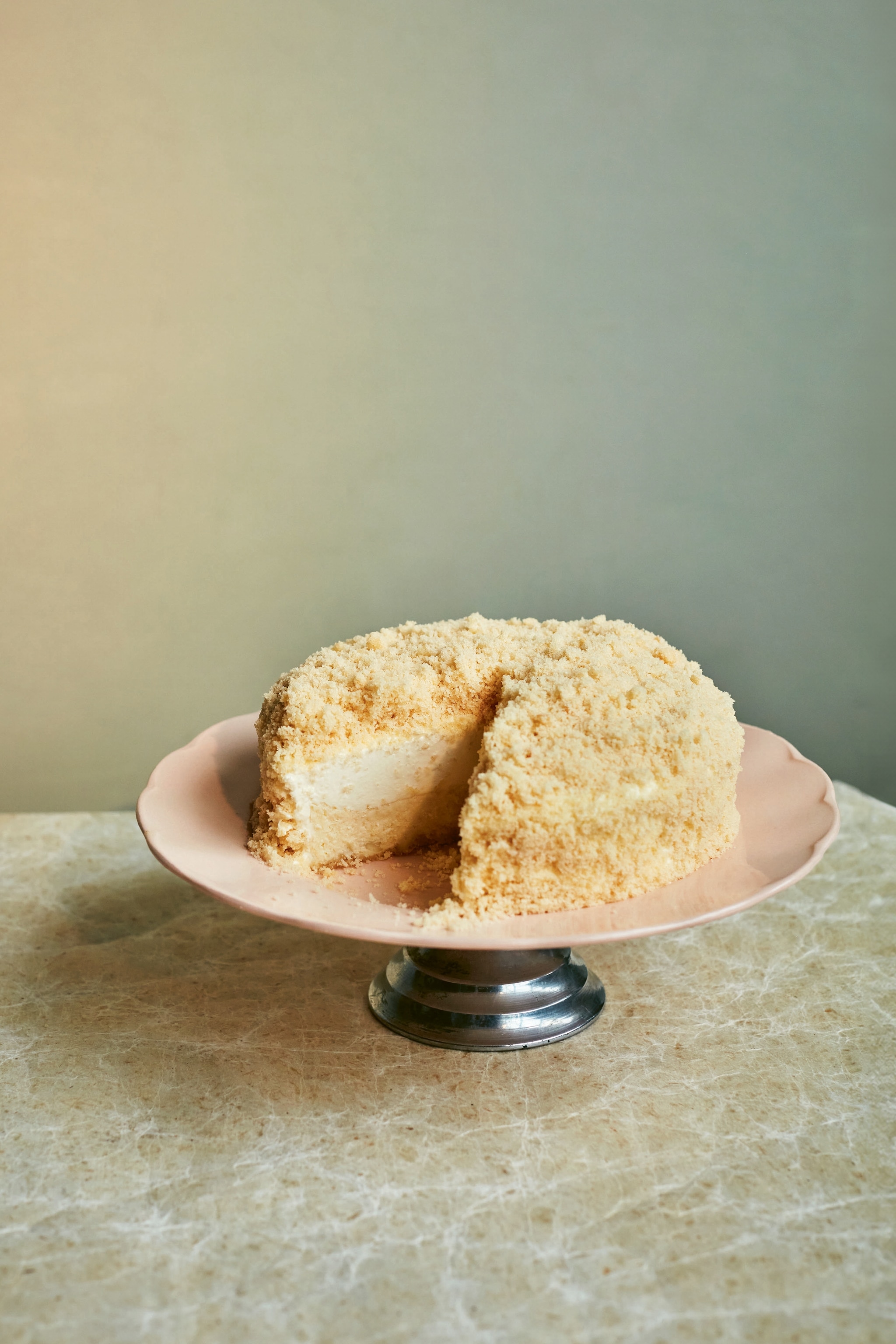 A round cheesecake on a cake stand with a piece missing.
