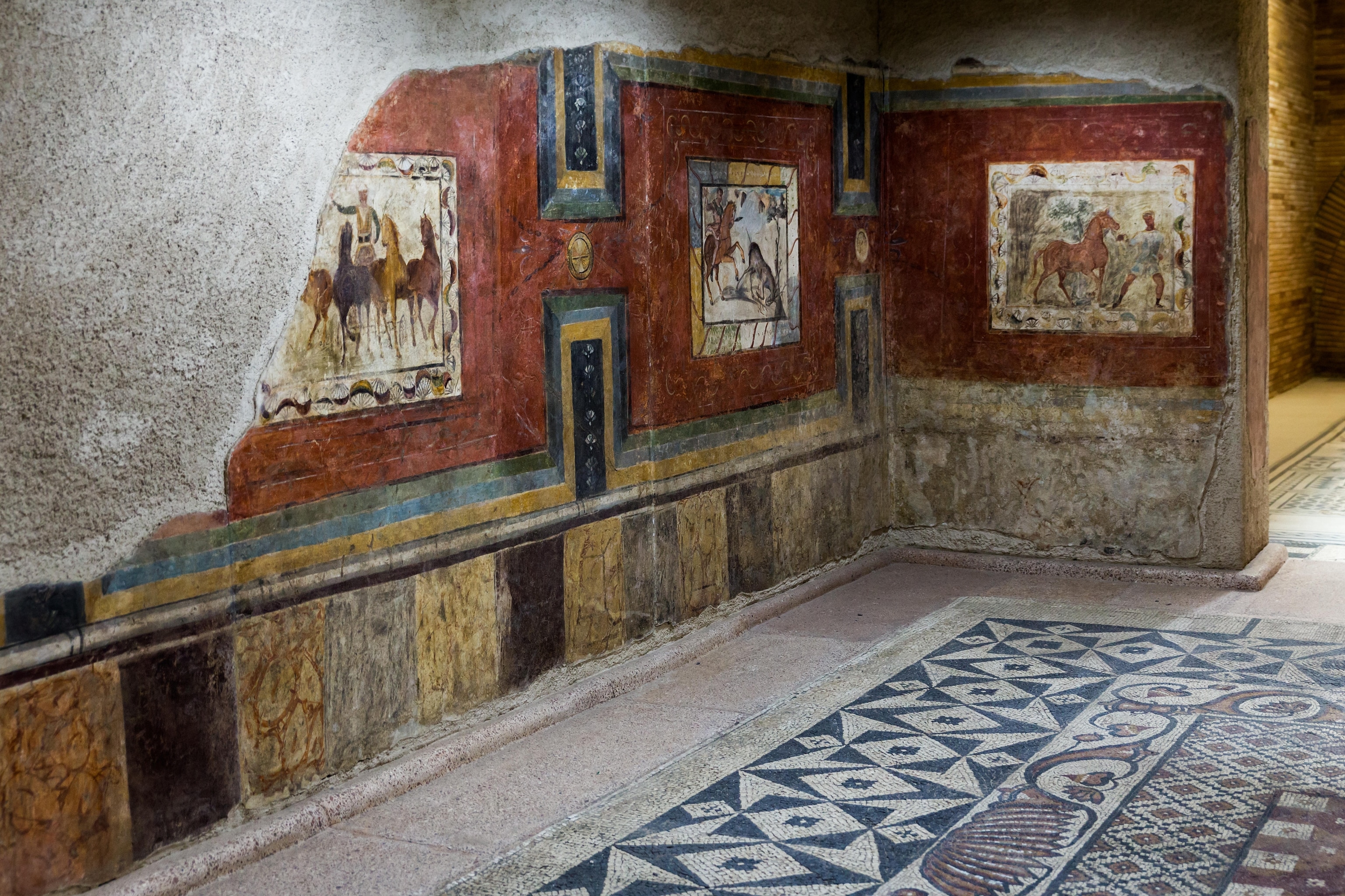 a room in a Roman house that features a ornamental mosaic floor and wall painting depicting circus and hunting scenes