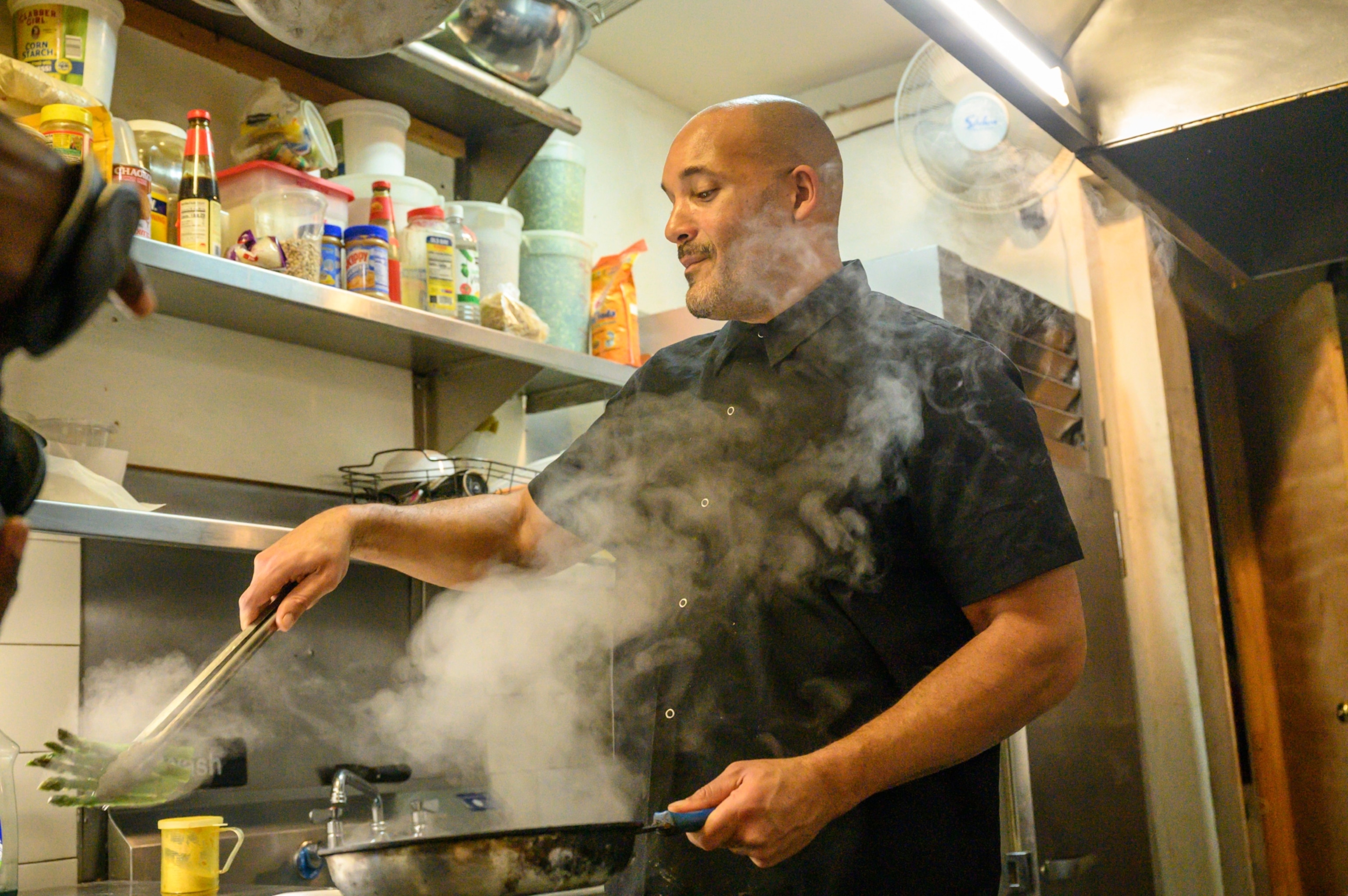 Man in a restaurant kitchen cooking as steam rises from the pan