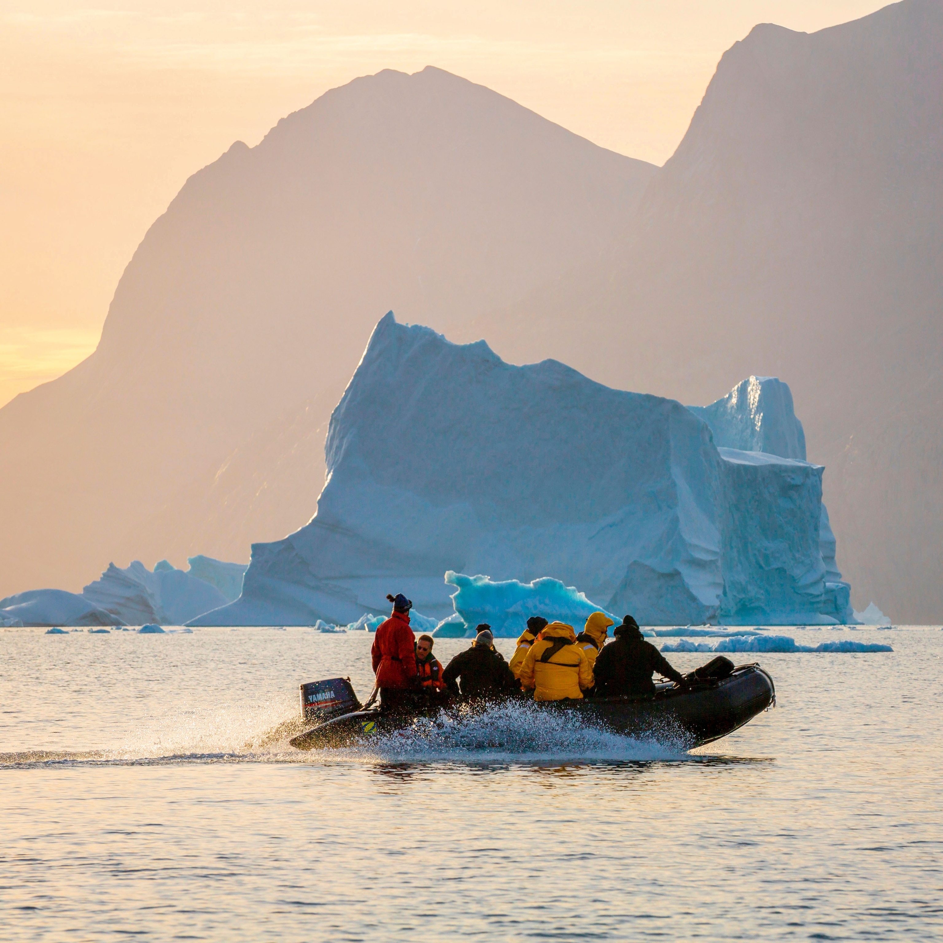 travellers aboard inflated boat with icerbergs in distance