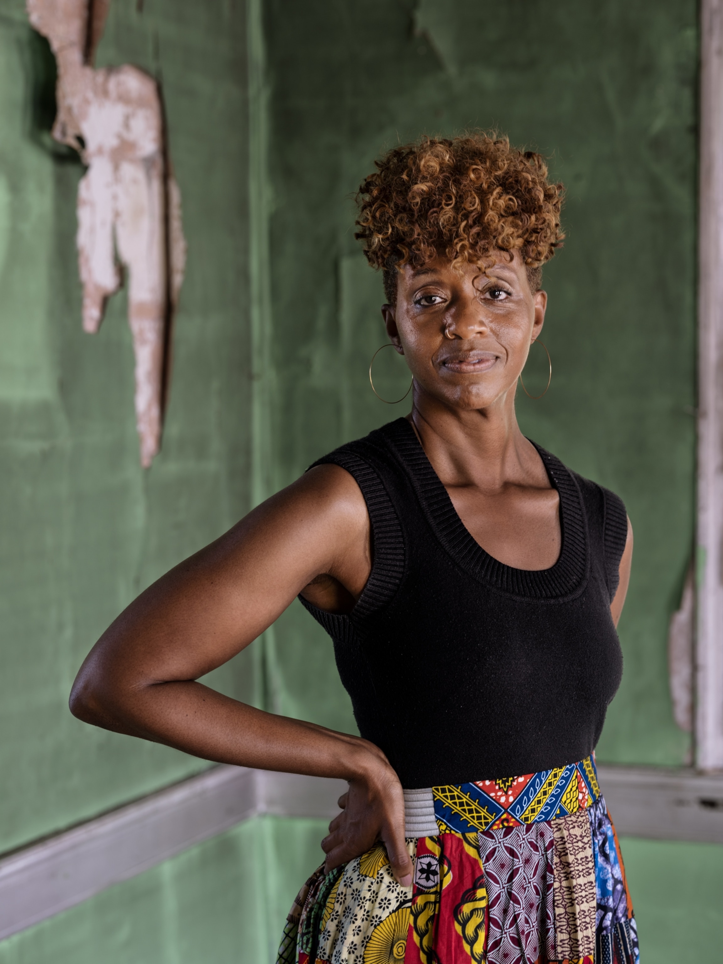 Picture of a woman in black top and colorful skirt standing for a portrait.