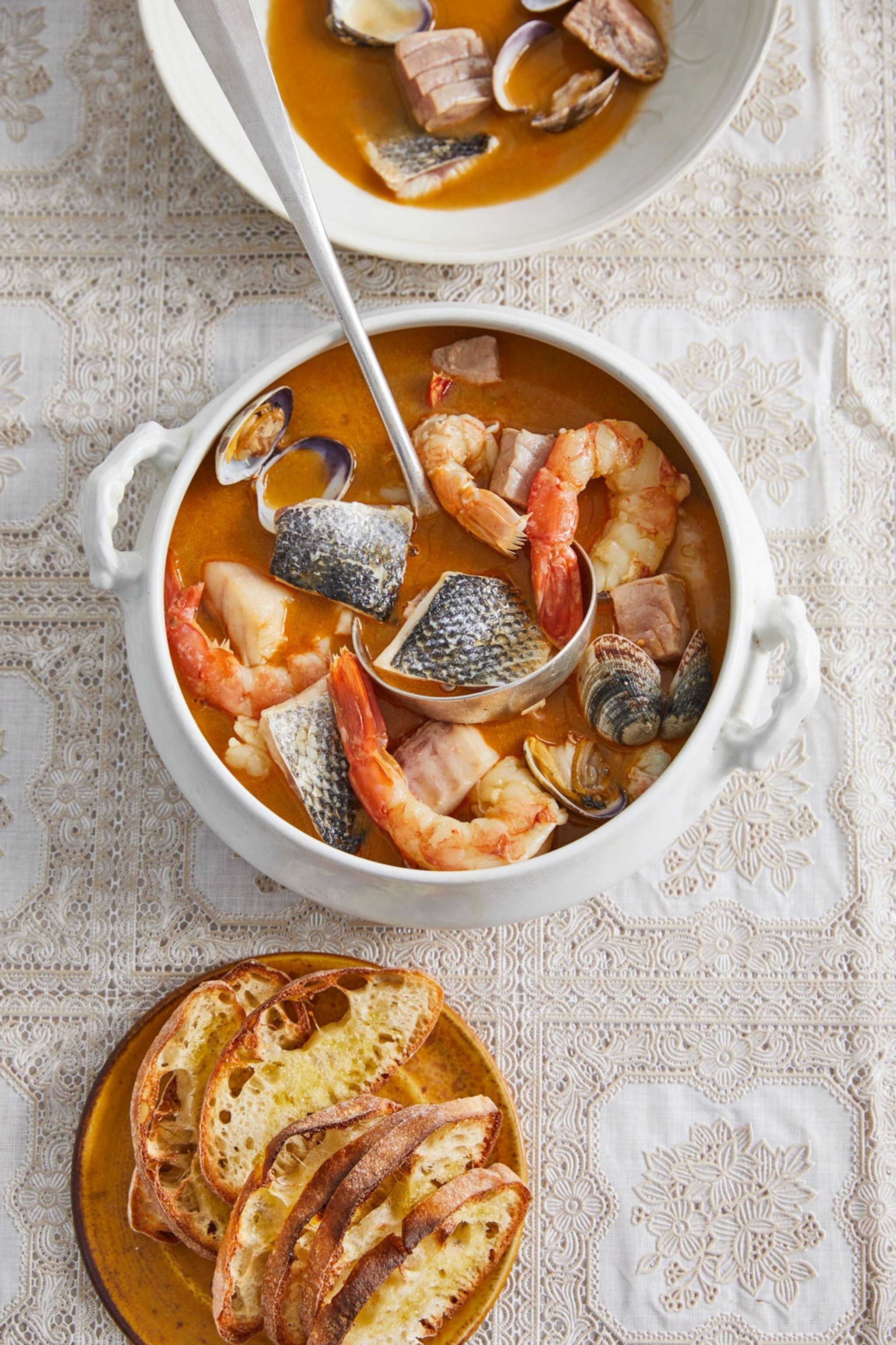 A bowl filled with a red broth and fish, with a serving spoon