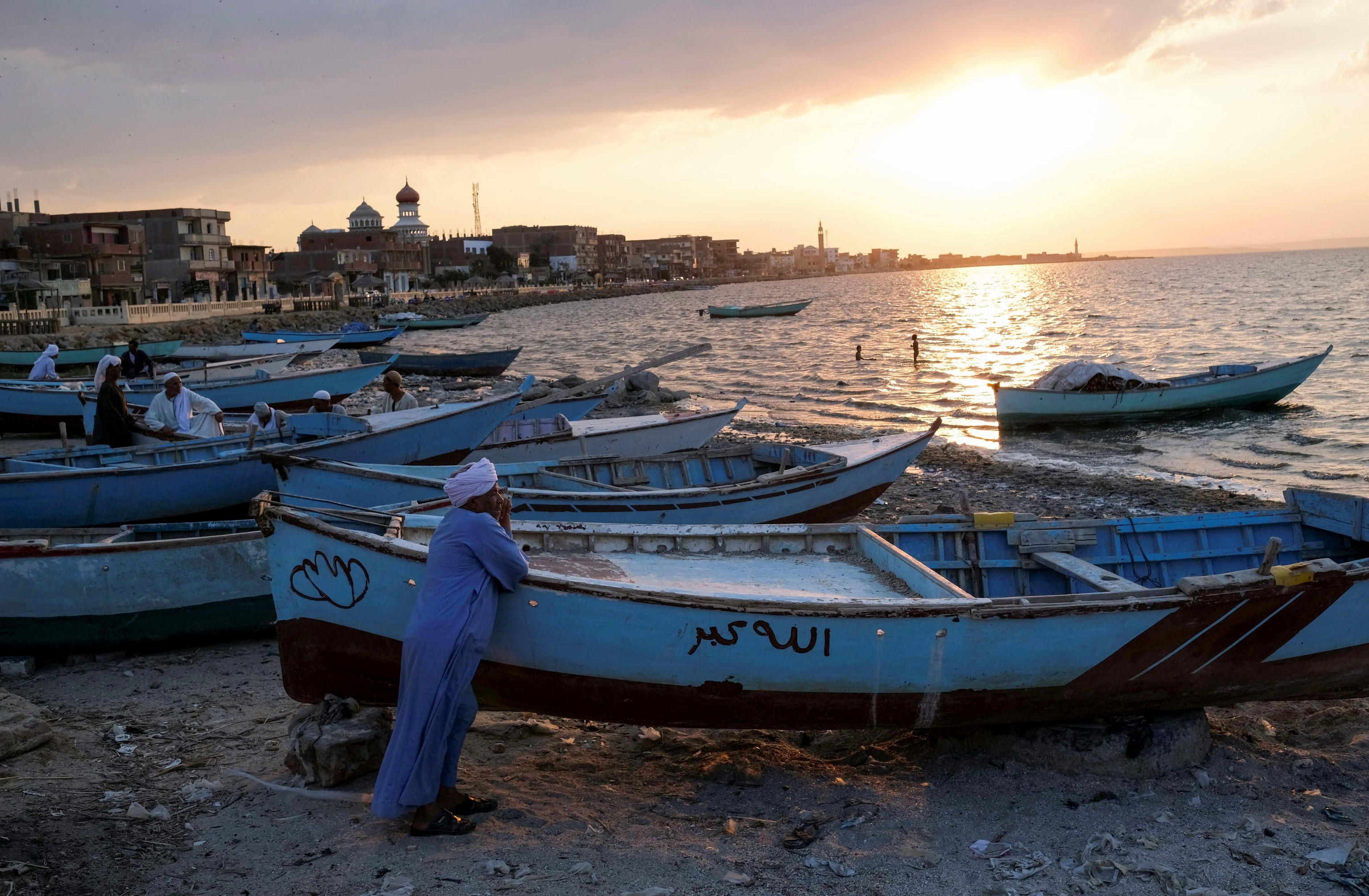 Fishermen stand next to their boats along the shore at Lake Qarun in the Ezbat Soliman