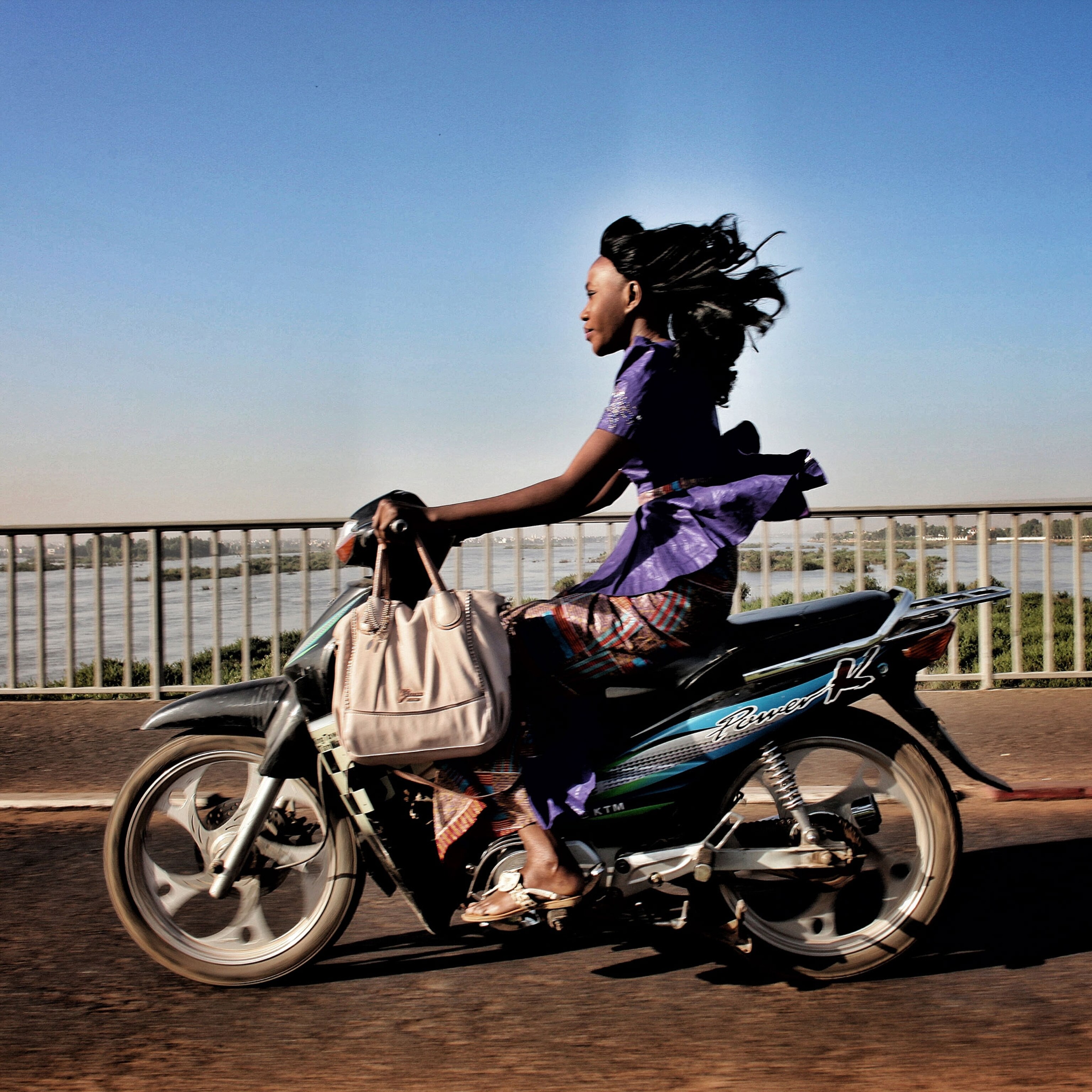 woman rides a motorbike on a bridge over the Niger River in Bamako, Mali