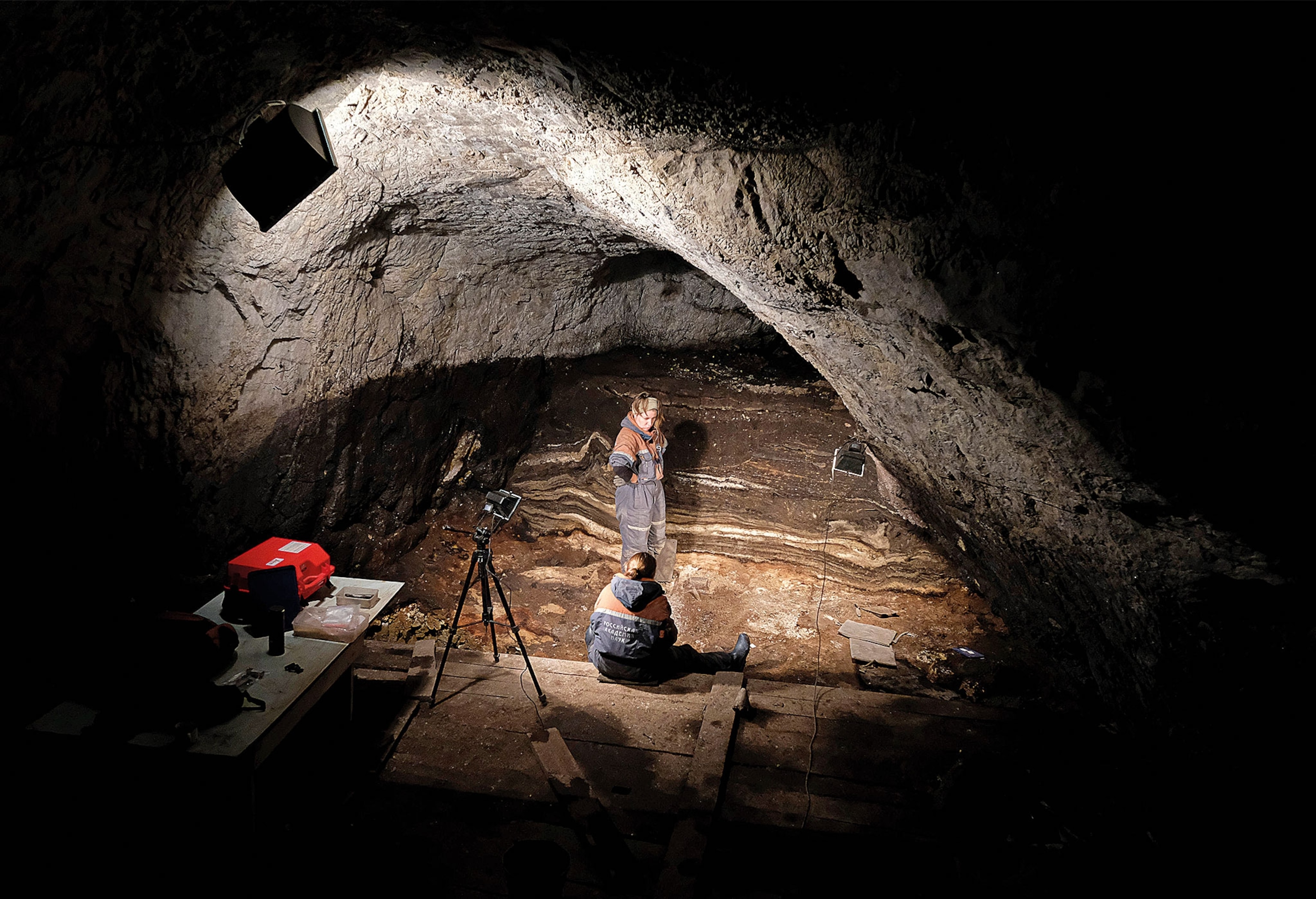 A view of 2 people sitting in a dark cave, lit by one light