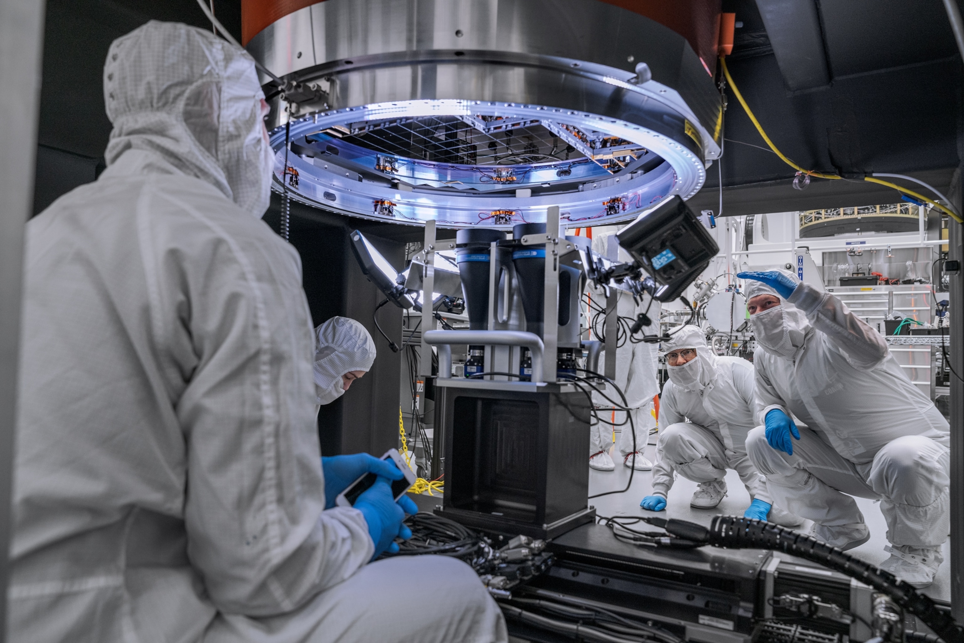 Picture of four people in white body suits and masks working on lard devise.