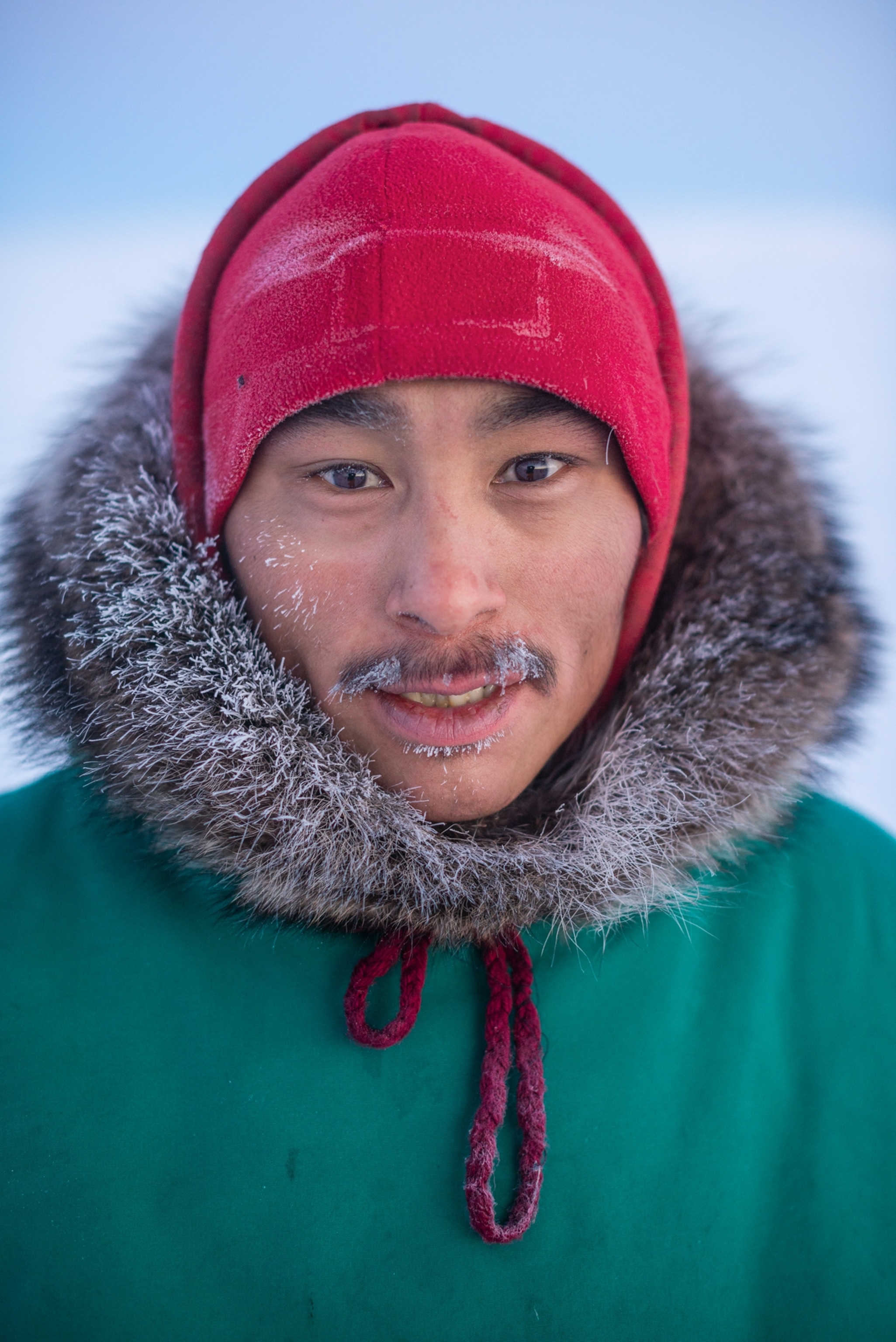 Inuit man in green parka and red hat.
