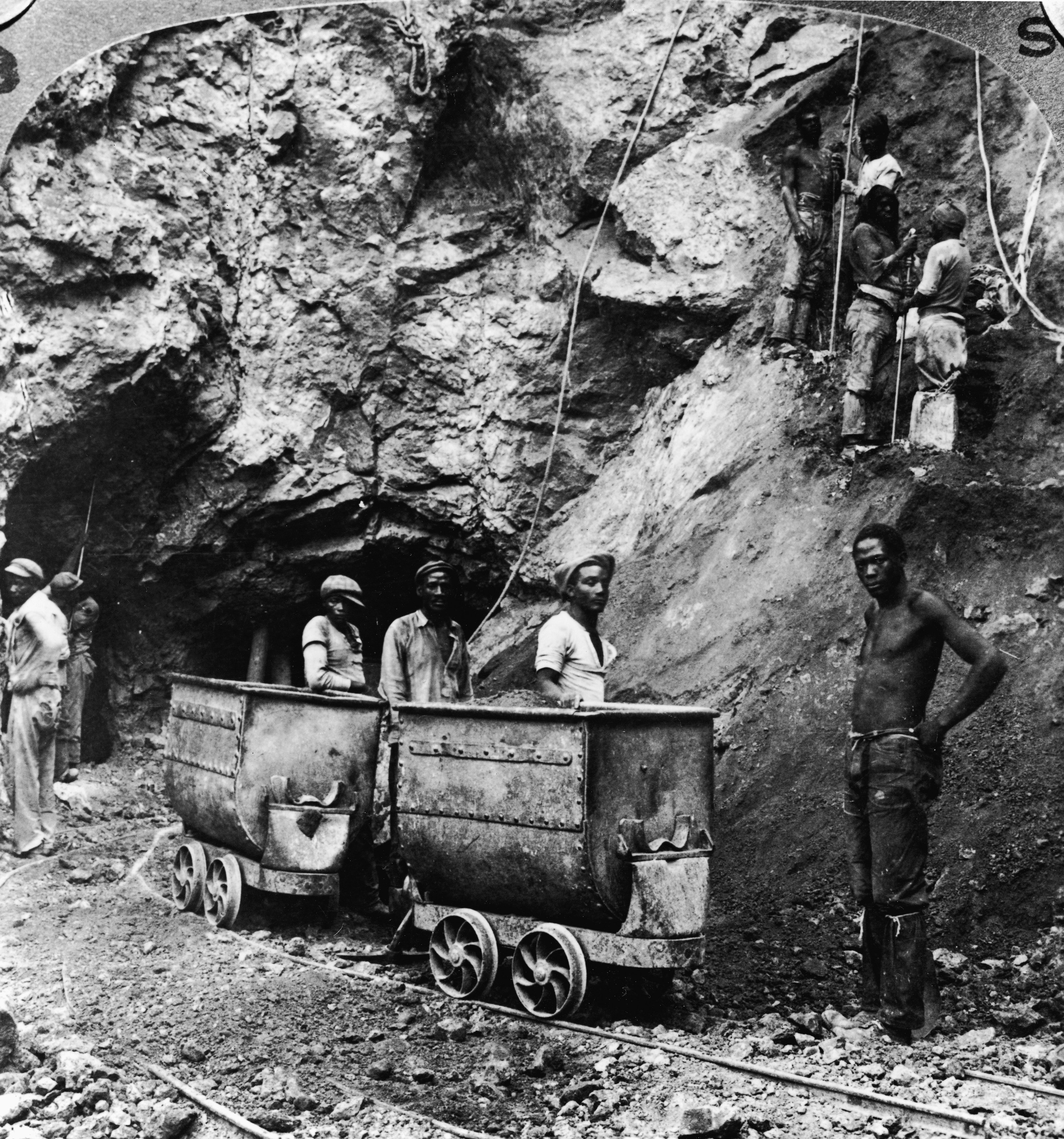 a black and white photograph of miners standing by a mine cart