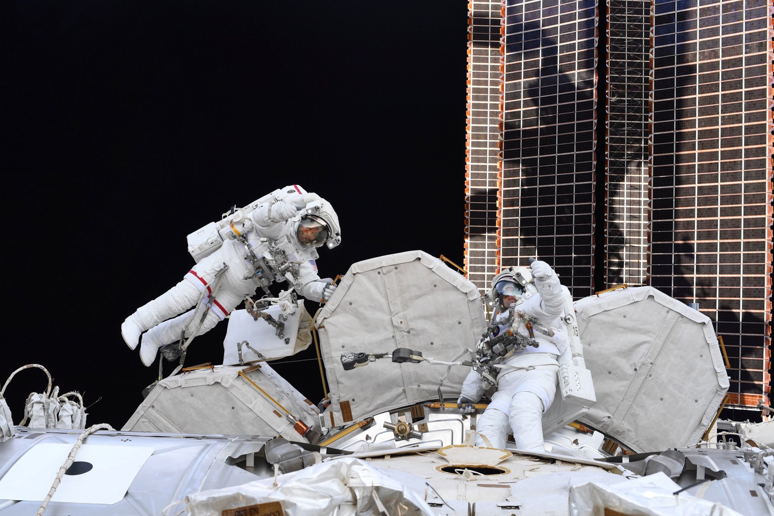 two astronauts in white suits in open space working on spacecraft.