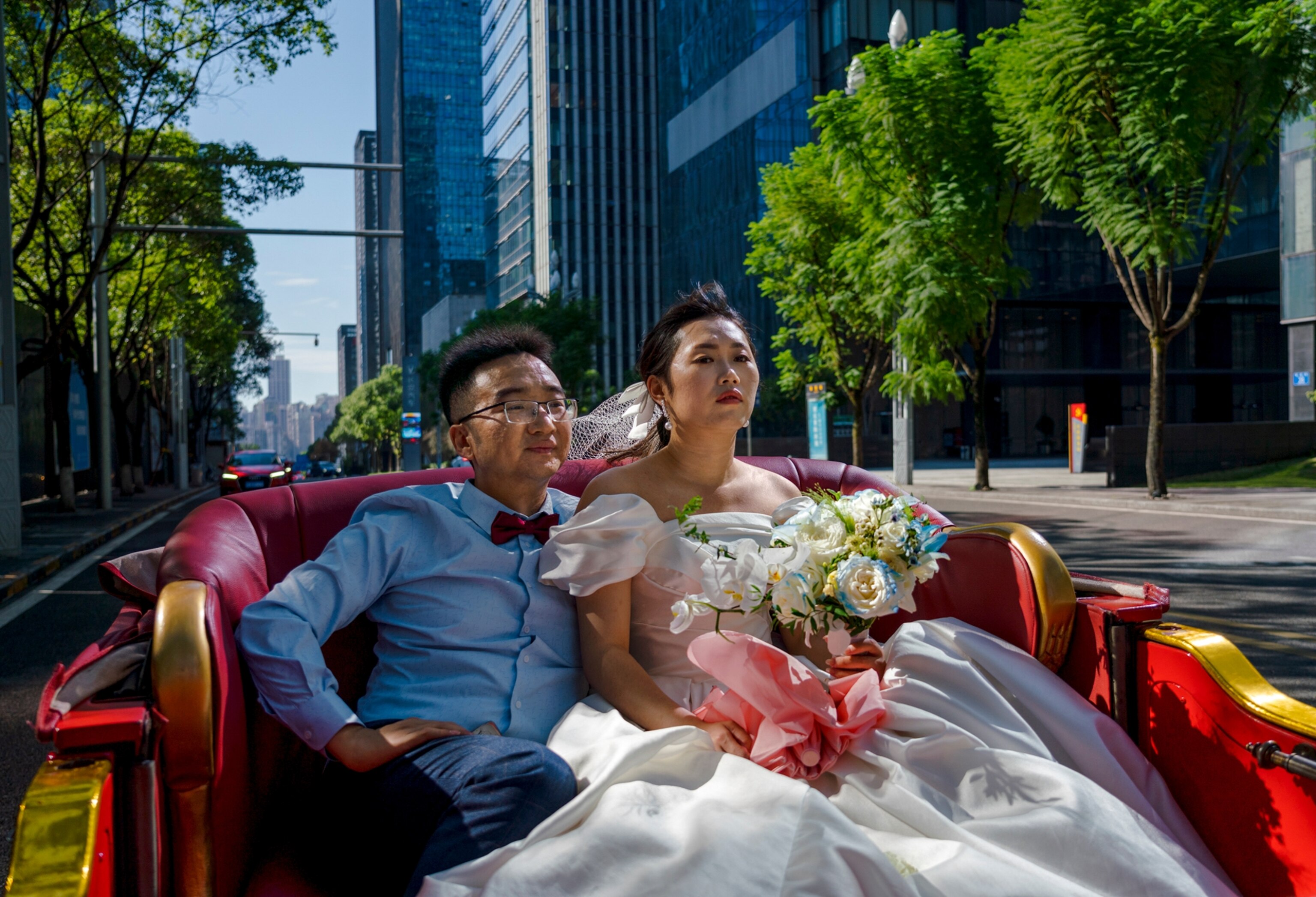 Picture of couple with the woman wearing a white wedding dress riding in a red and gold chariot through the metropolitan streets.