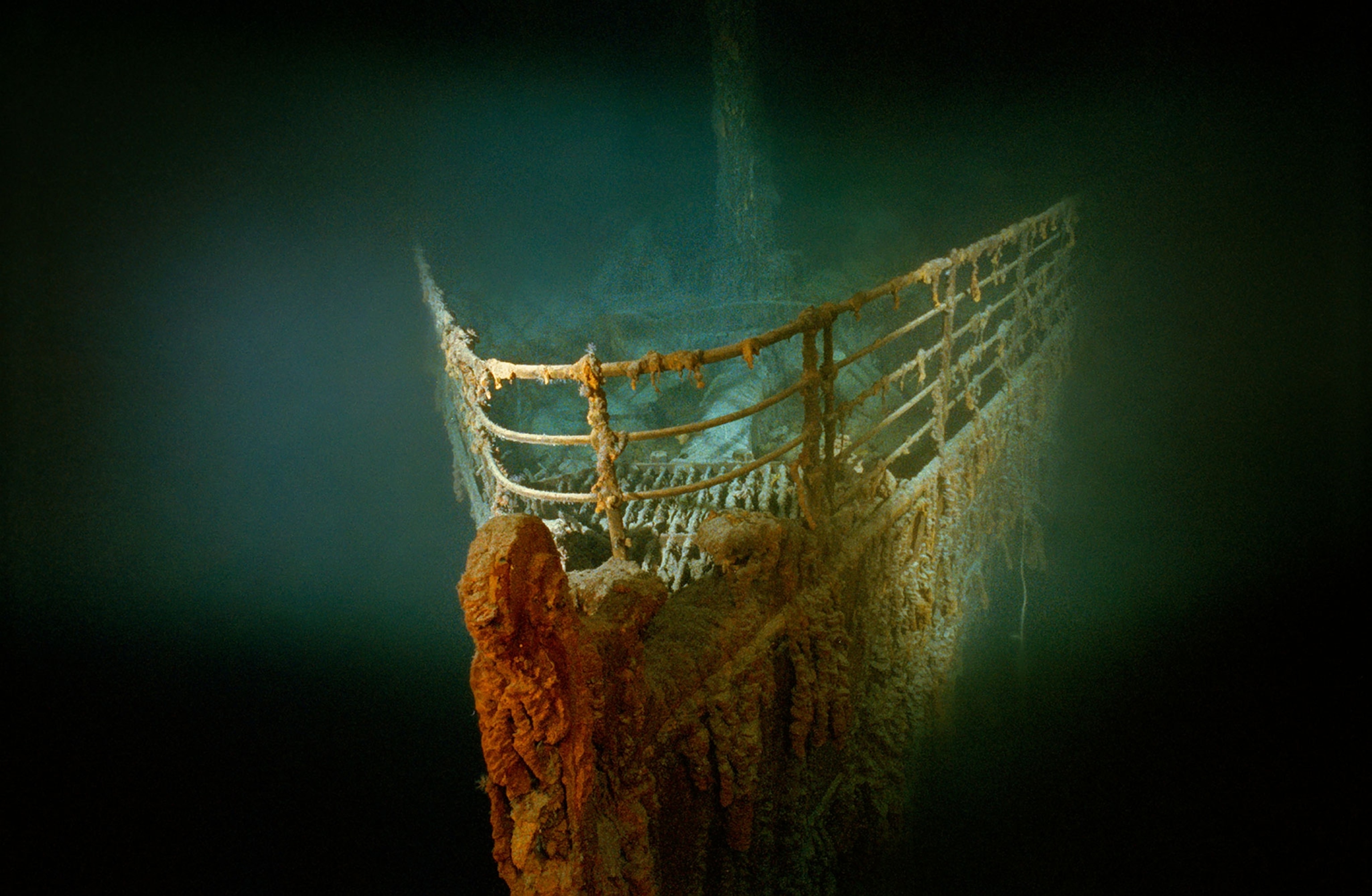 Looking down at the front of the rusting Titanic underwater. The ship is lit while the surrounding water is completely dark.