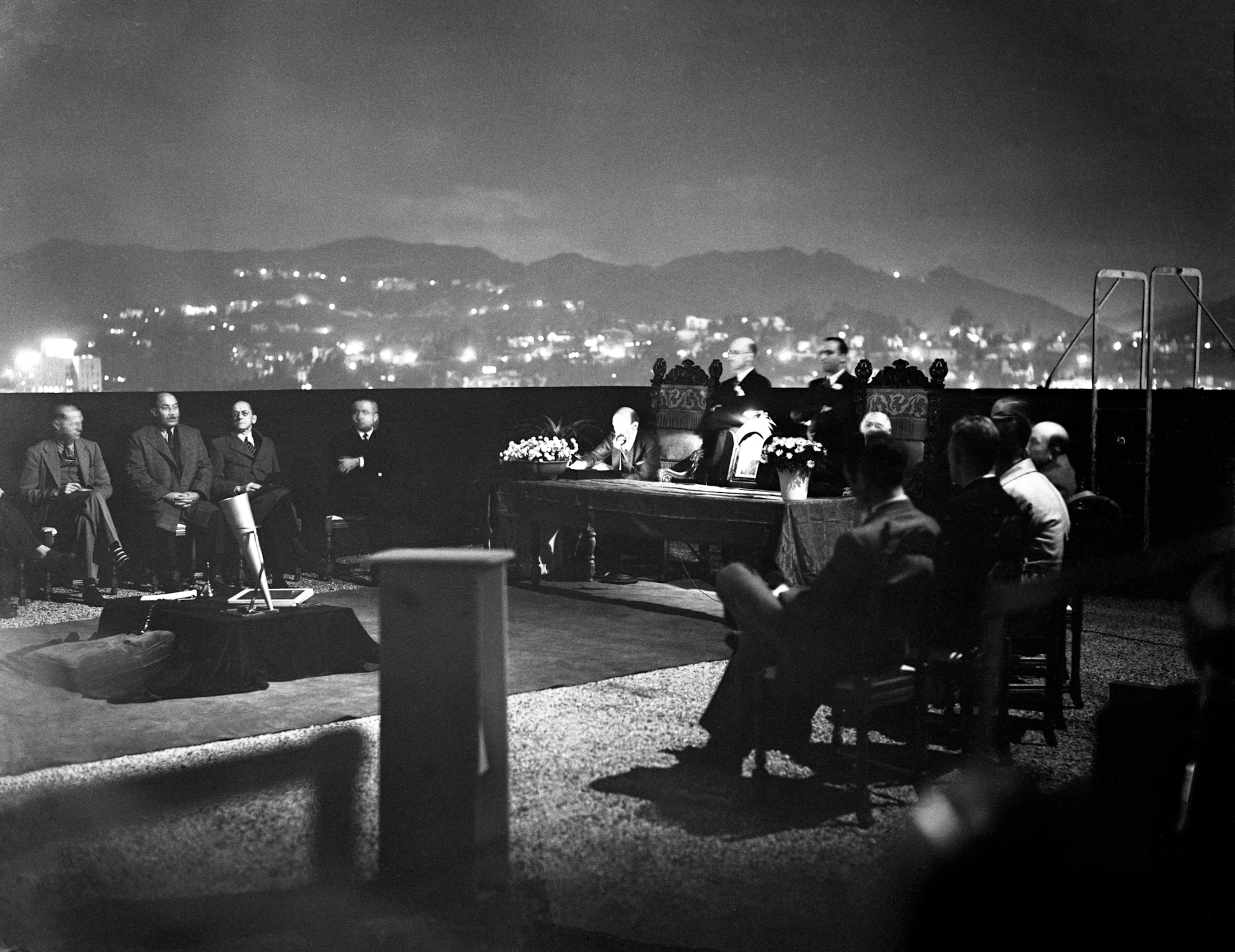 A group seated atop a hotel in Hollywood at night, as they attempt a séance to communicate with Houdini.