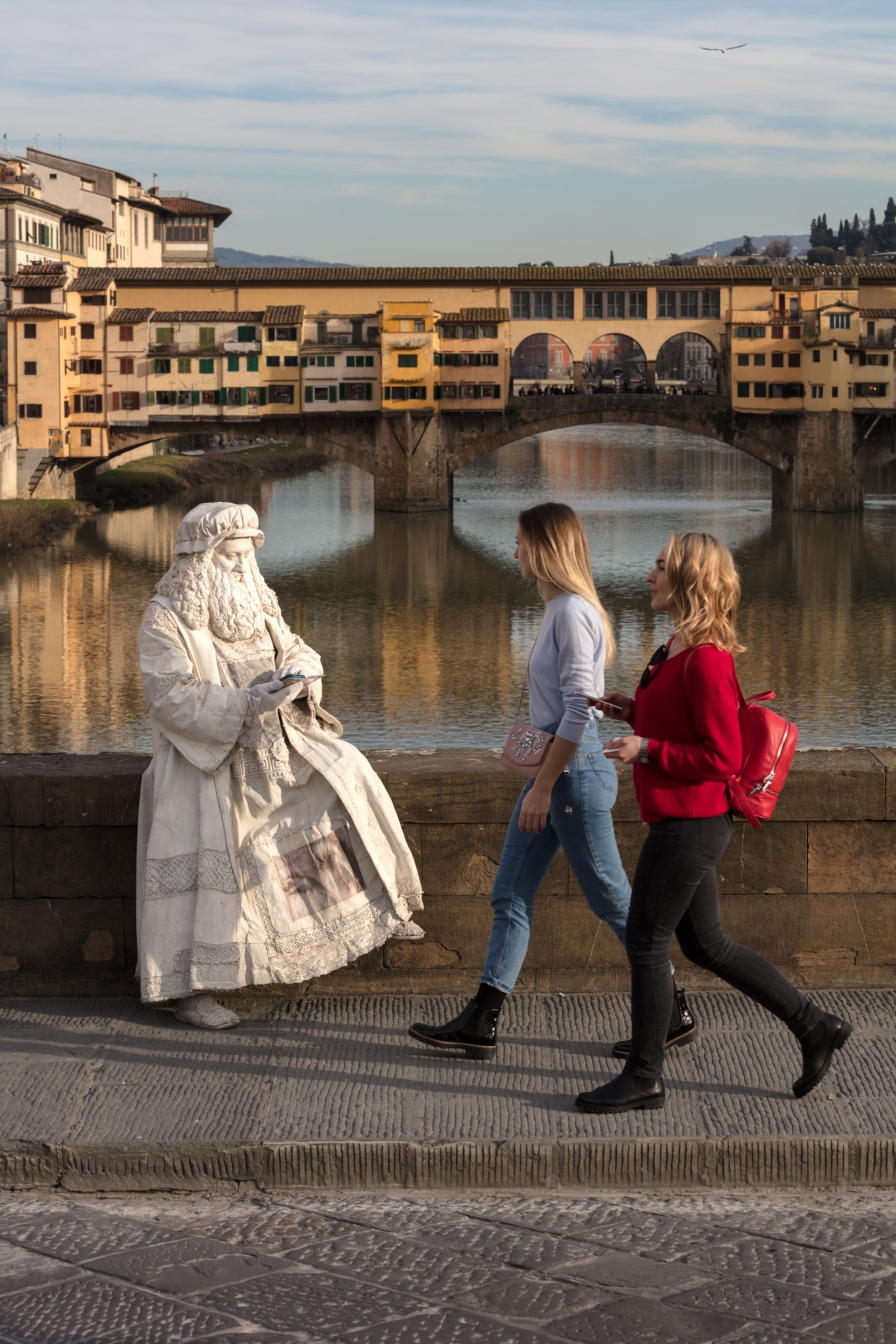 a Renaissance impersonator in looking at phone near a bridge as two woman walk by