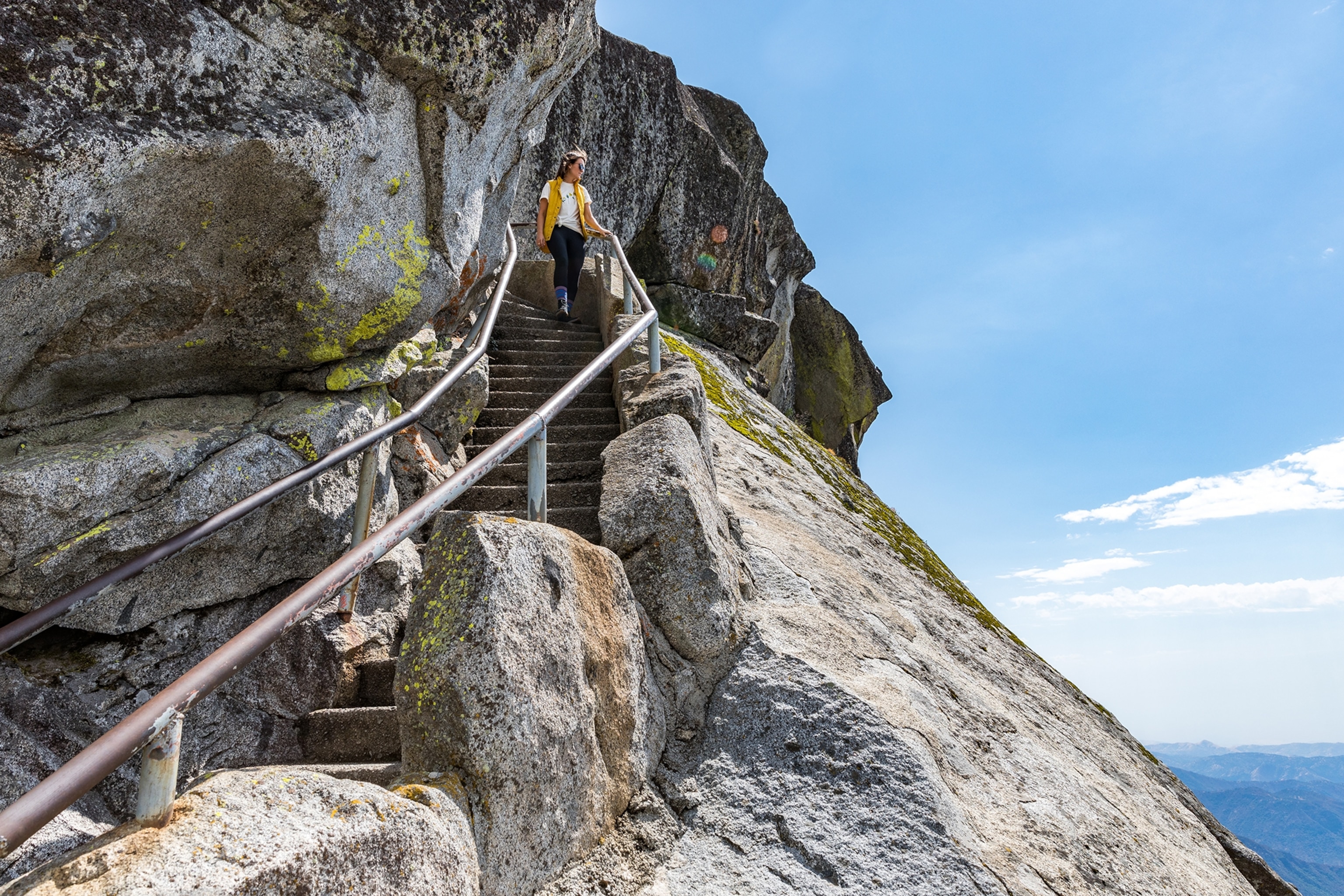 A woman walking down stairs on a rockface at Moro Rock in Sequoia National Park, California.