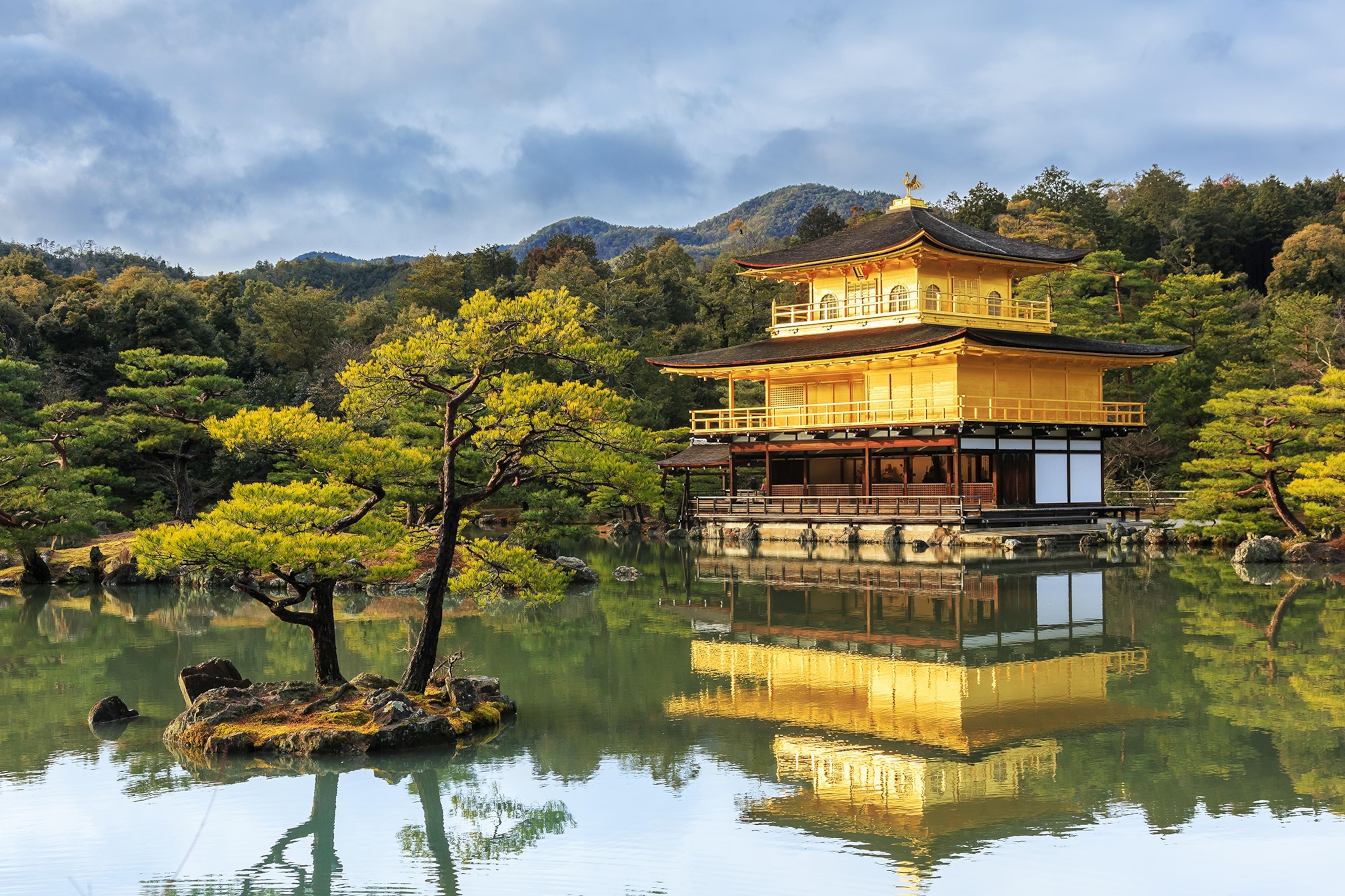 Japanese temple sits on the water surrounded by green and yellow trees