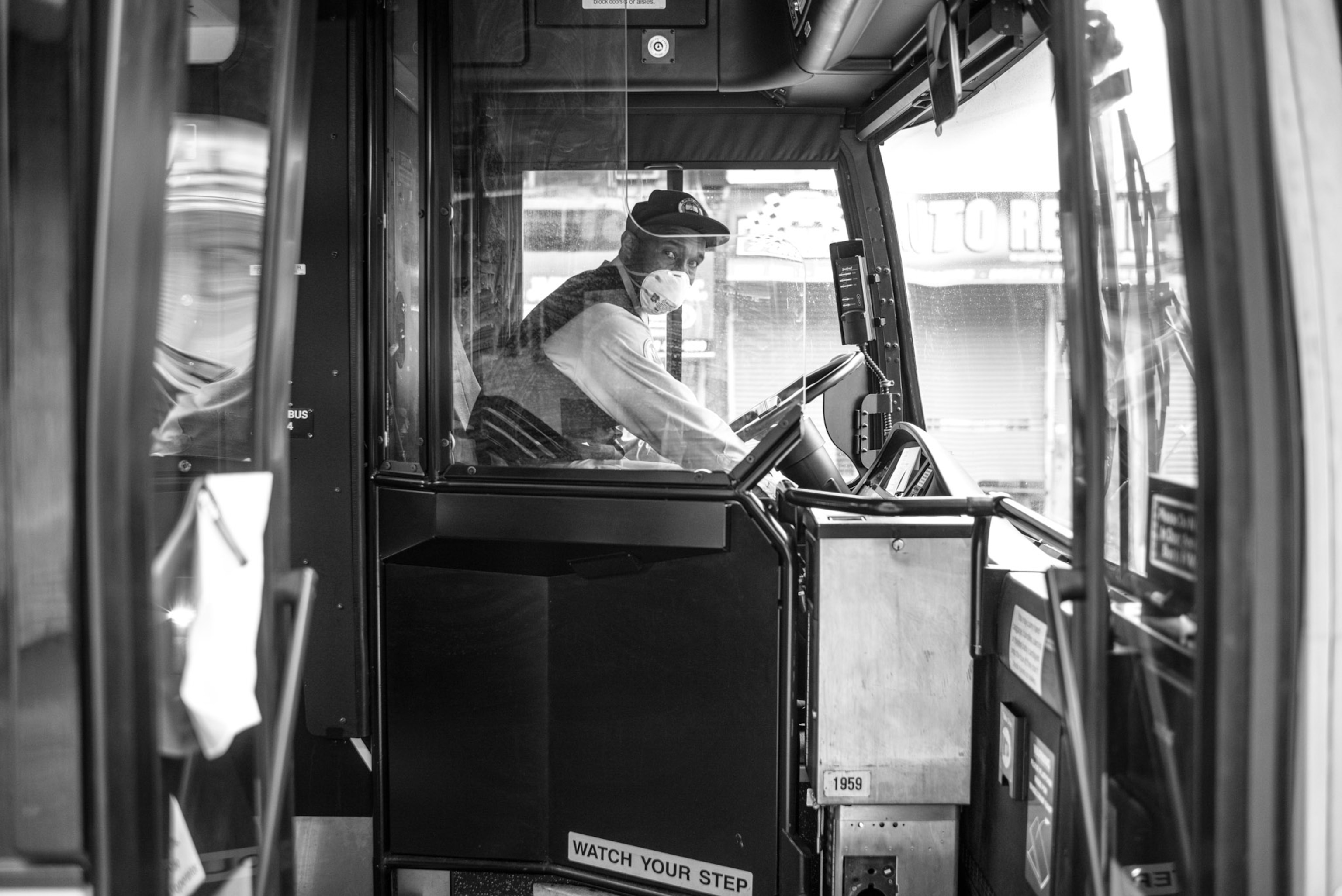 a bus driver wearing a mask in the front seat of a bus