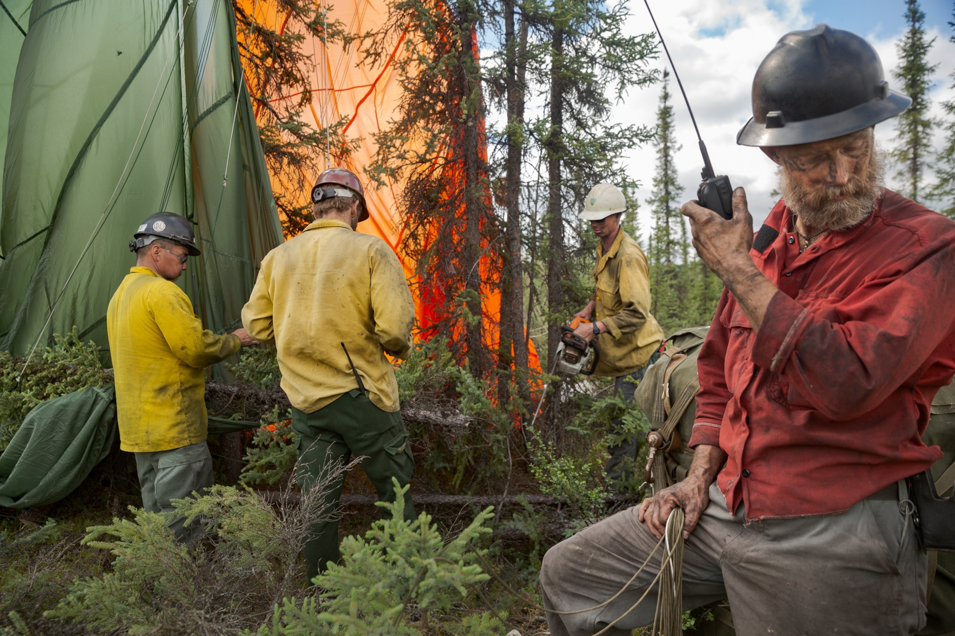 a man in red jacket on a radio phone and men in yellow jackets behind him