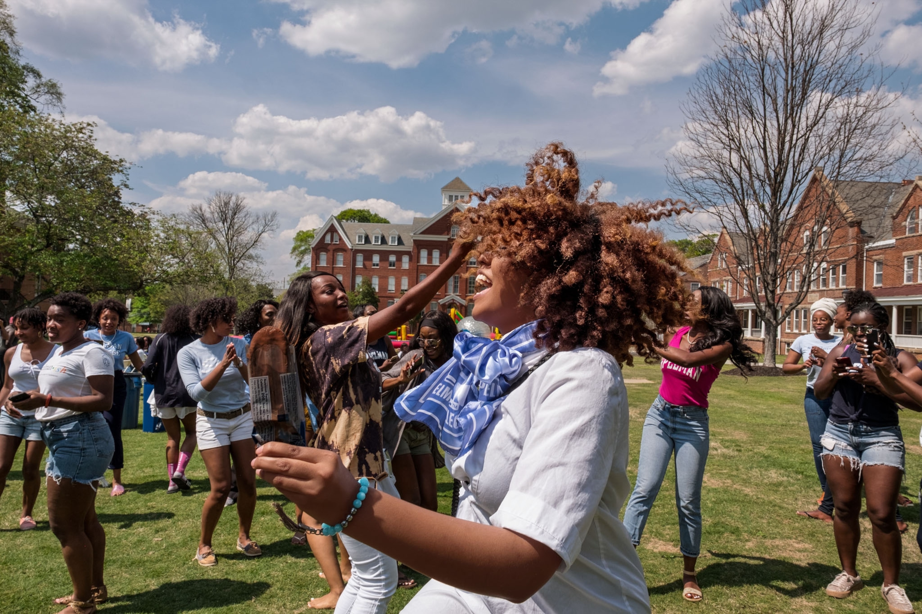 a young black woman dancing out on a campus lawn on a sunny day with other girls