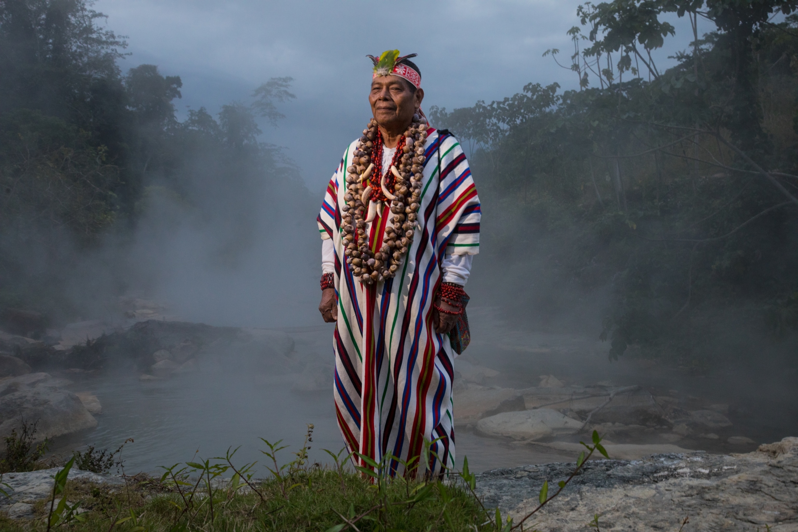 a shaman posing for a portrait on the banks of a misty river
