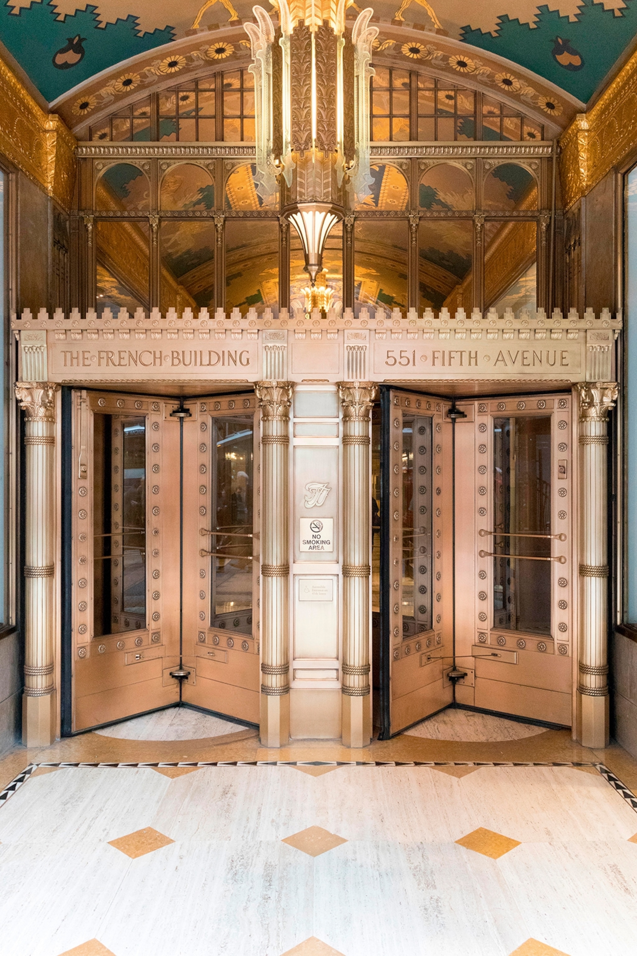 The entrance hall of a double swing-doored, art deco building in copper with decorative features.