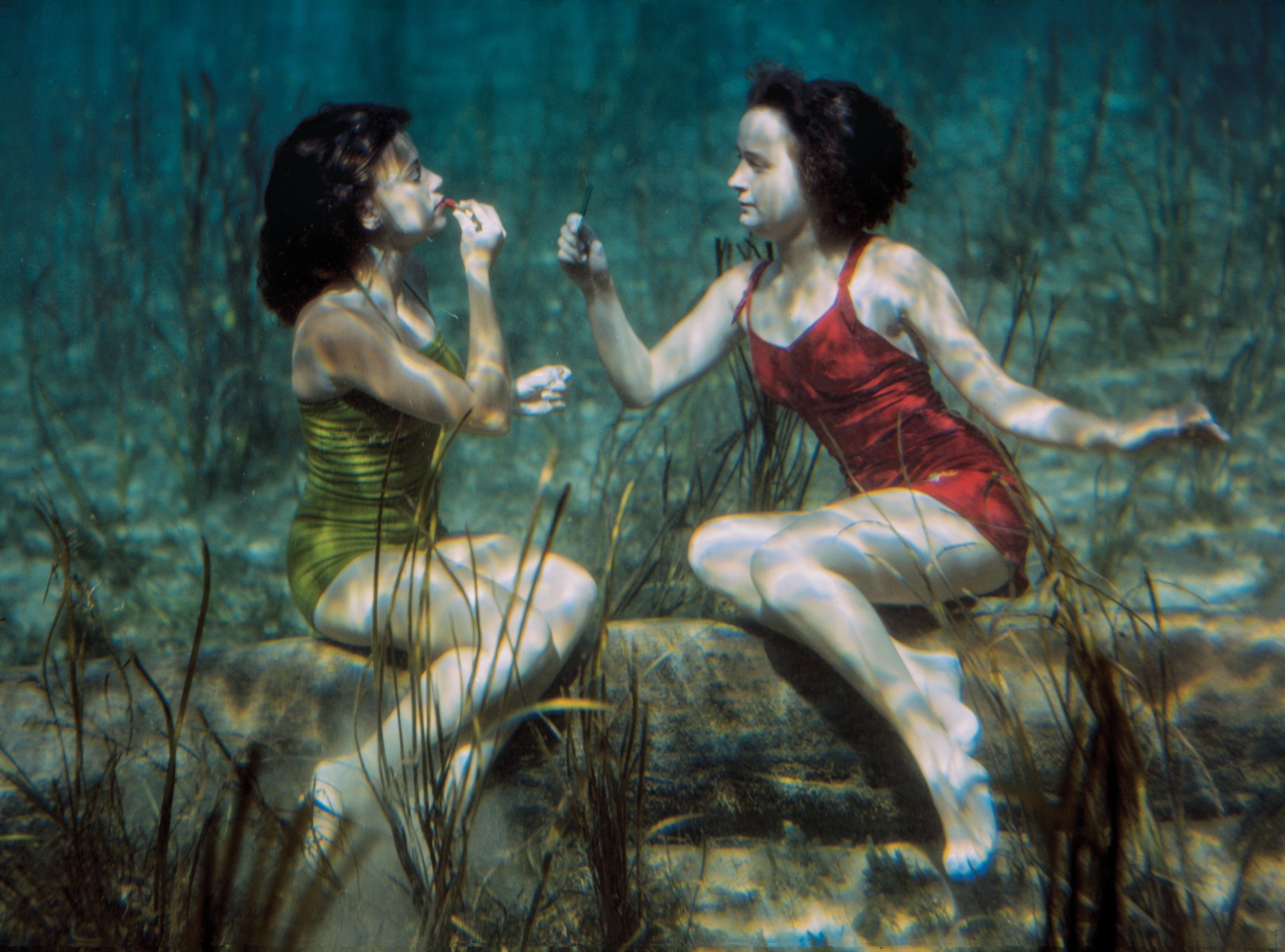 two young women applying lipstick while sitting underwater.