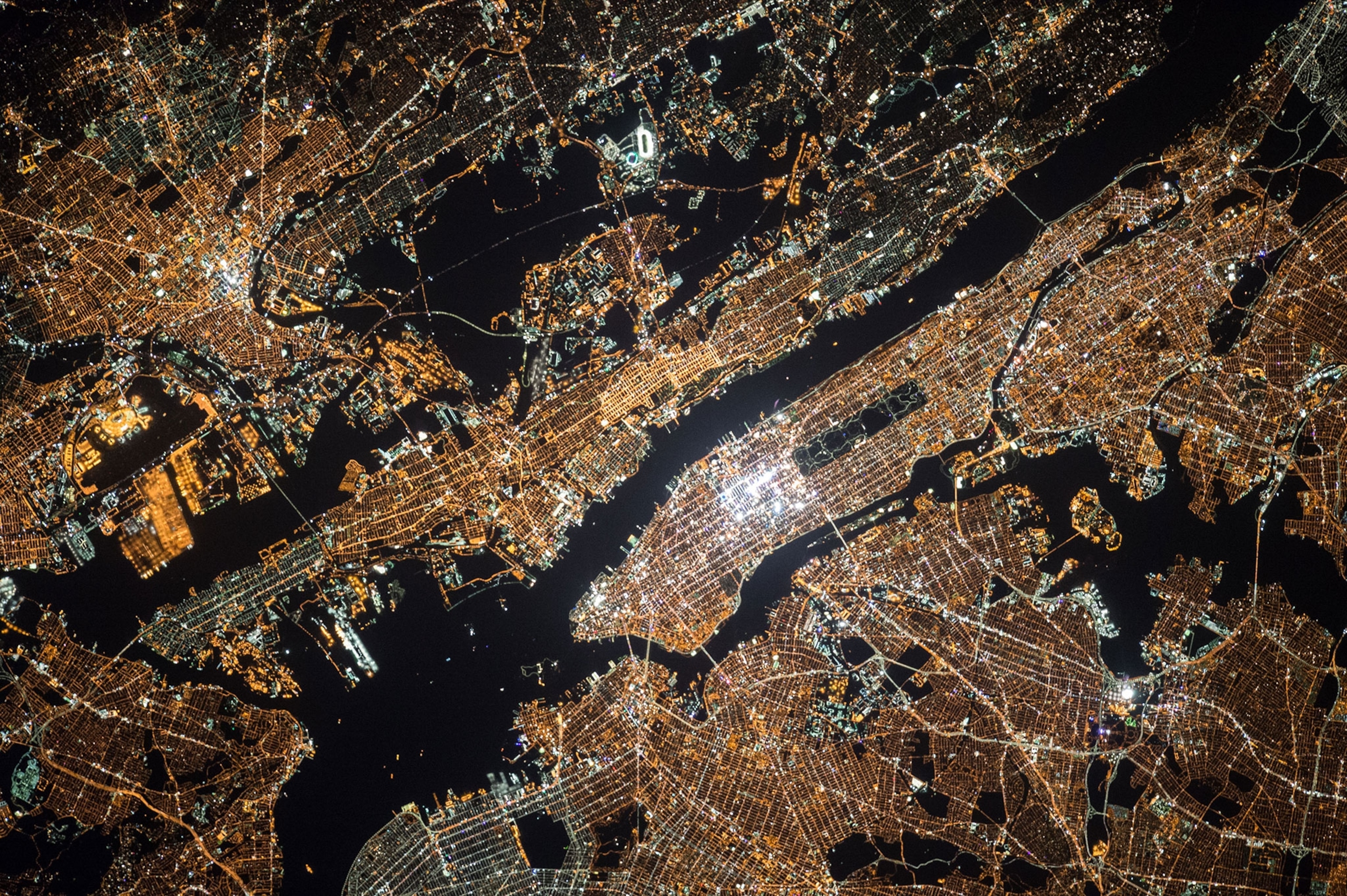 New York City at night, seen from the International Space Station, with the bright, white lights of Midtown Manhattan in the center of the image.