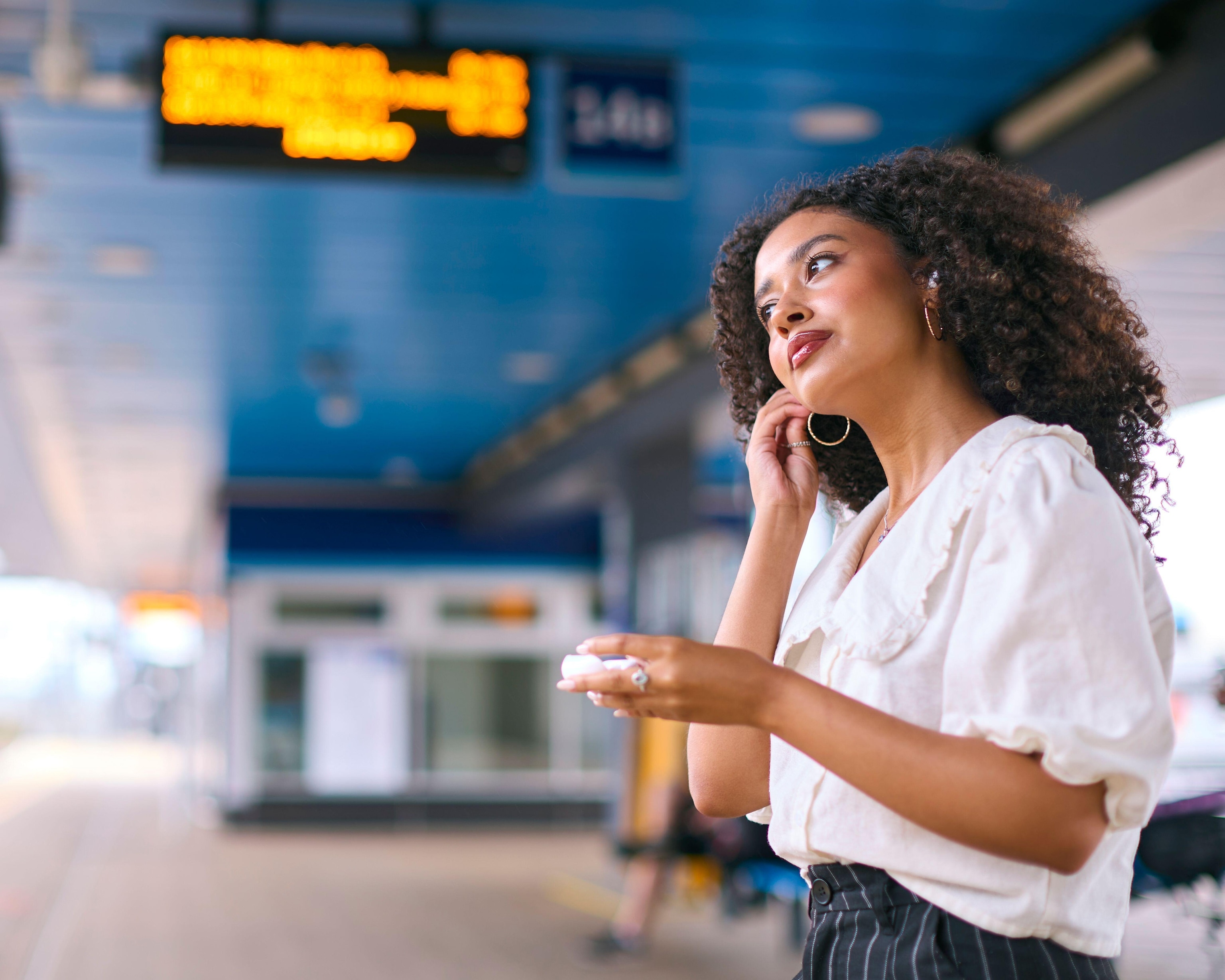 Businesswoman Commuting On Train Platform Putting In Wireless Earbuds