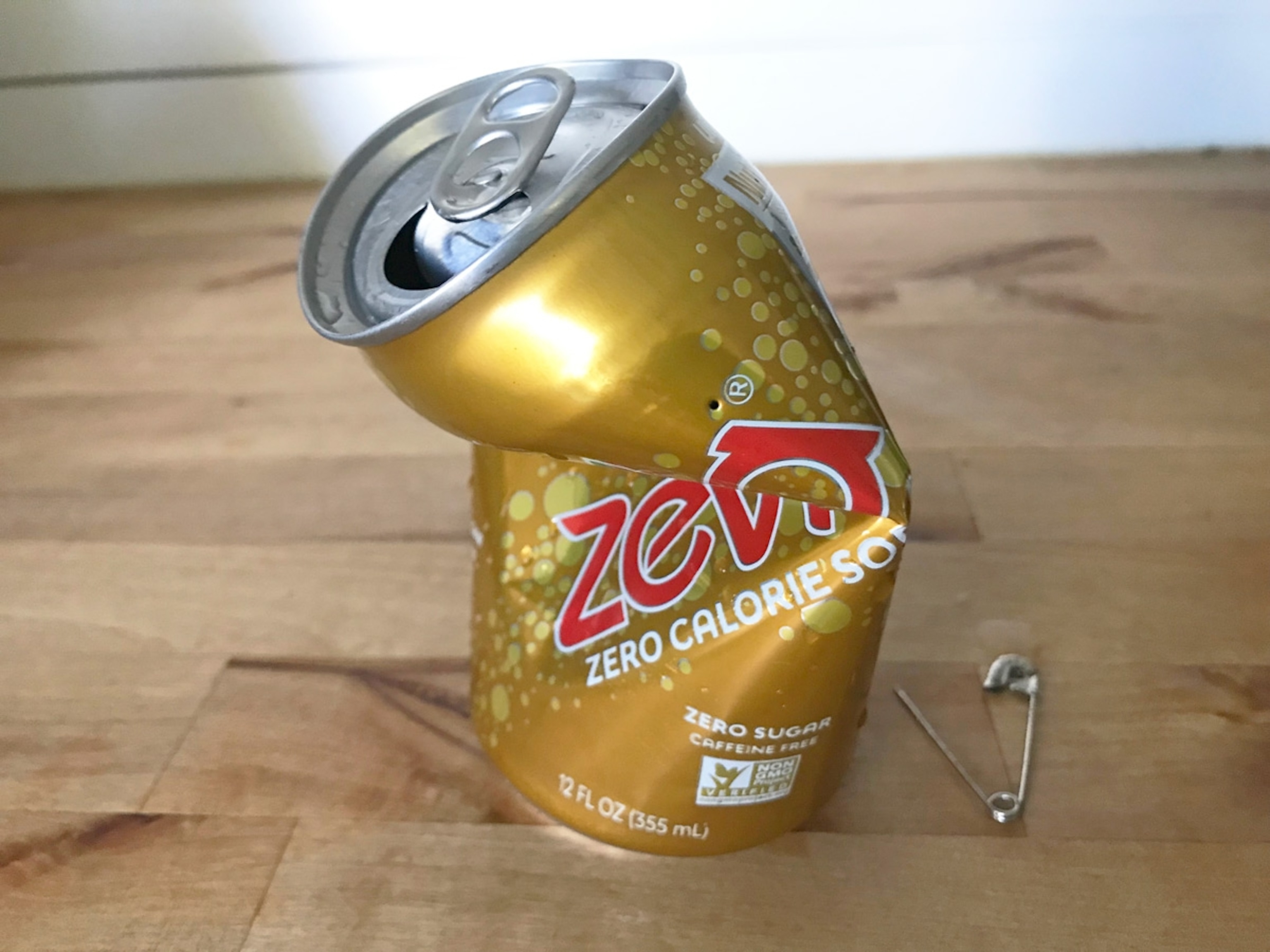A partially crushed can of soda with a hole pierced in the top.