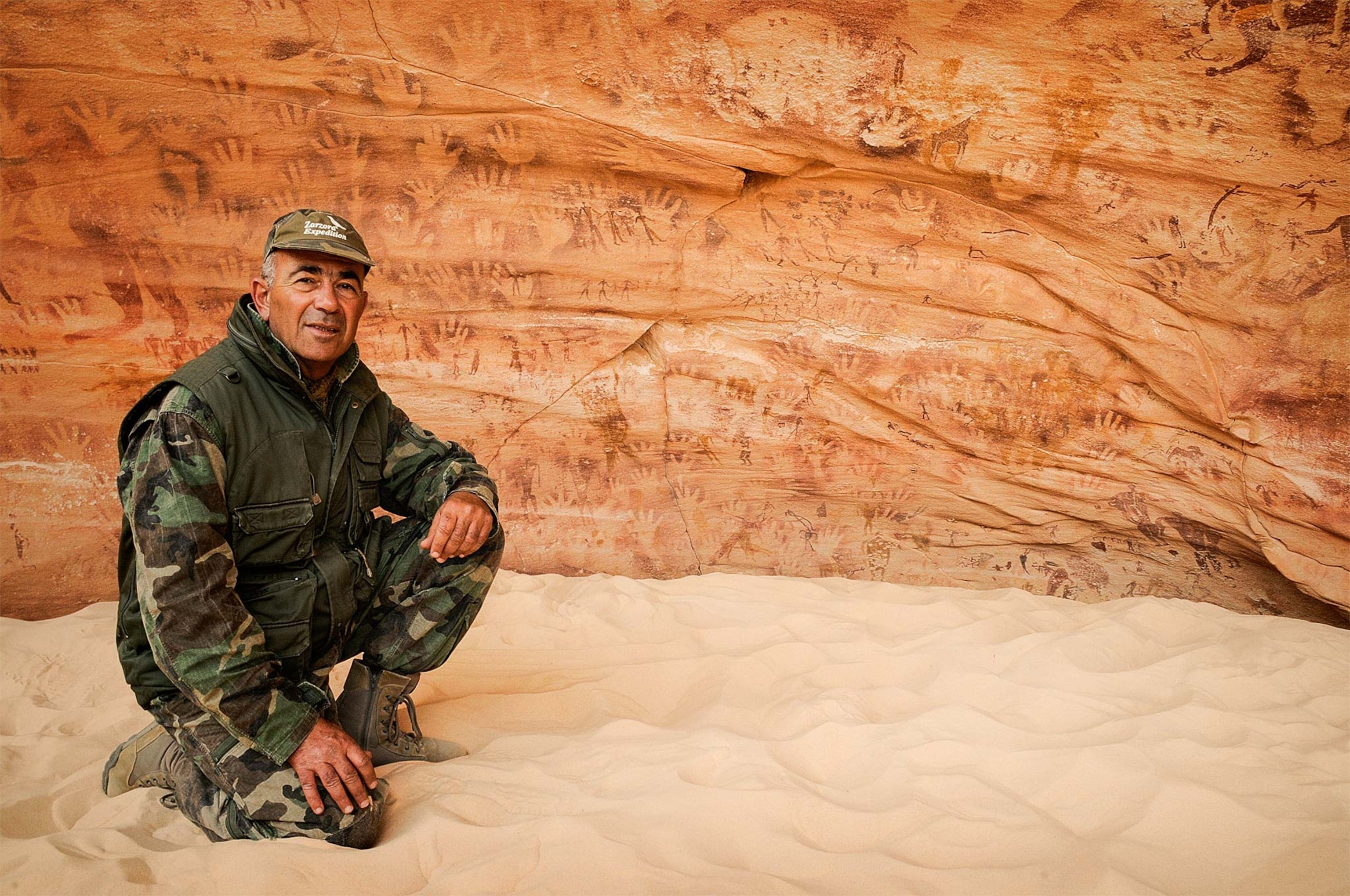 Archaeologist Ahmed Mestikawi squats before the handprint images on the Cave of Beasts.