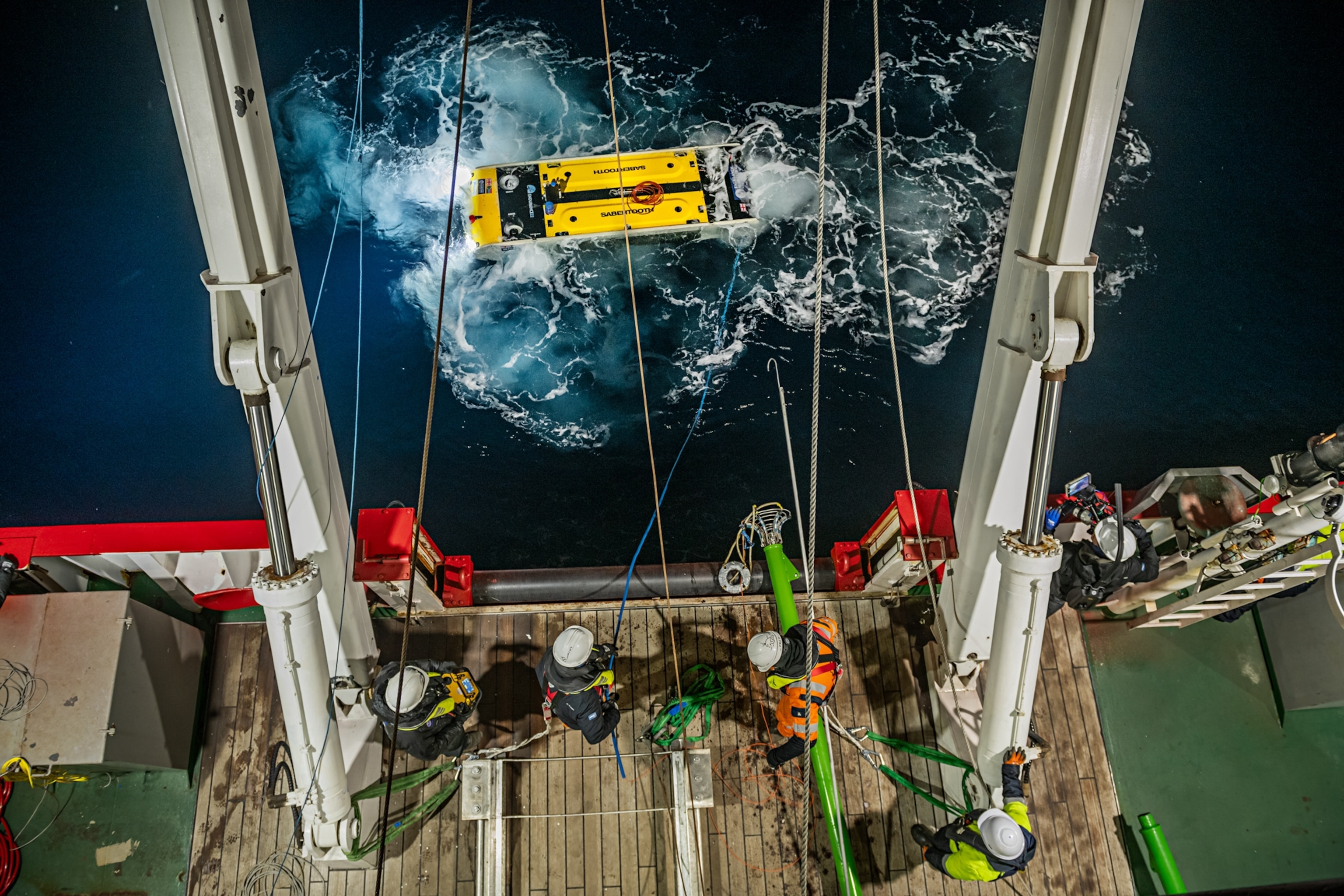 Members of the Endurance22 subsea team maneuver the Saab Sabertooth into position at the stern of the ship to hoist it back on board.