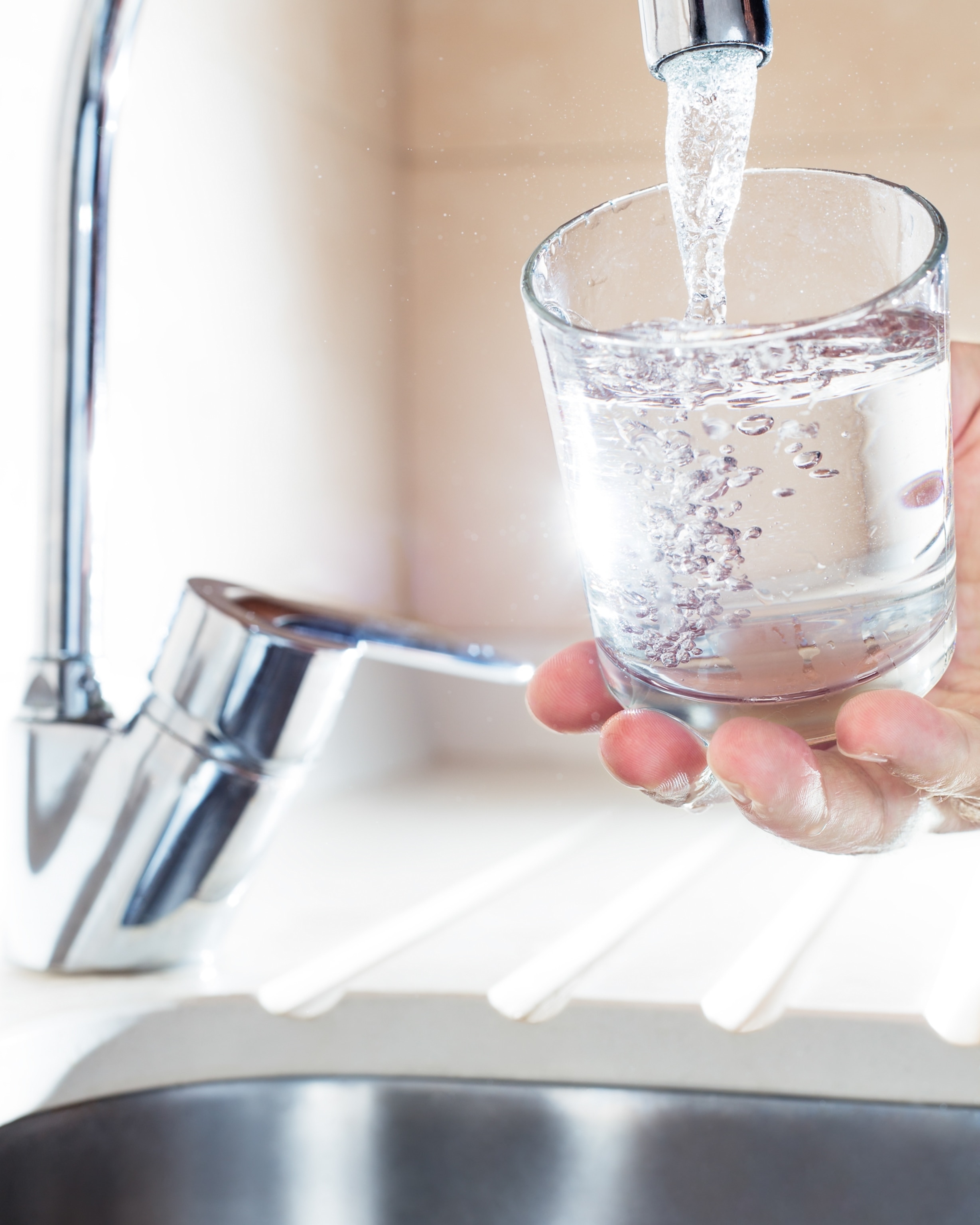 A close-up view of a person filling a glass of water from a kitchen faucet.