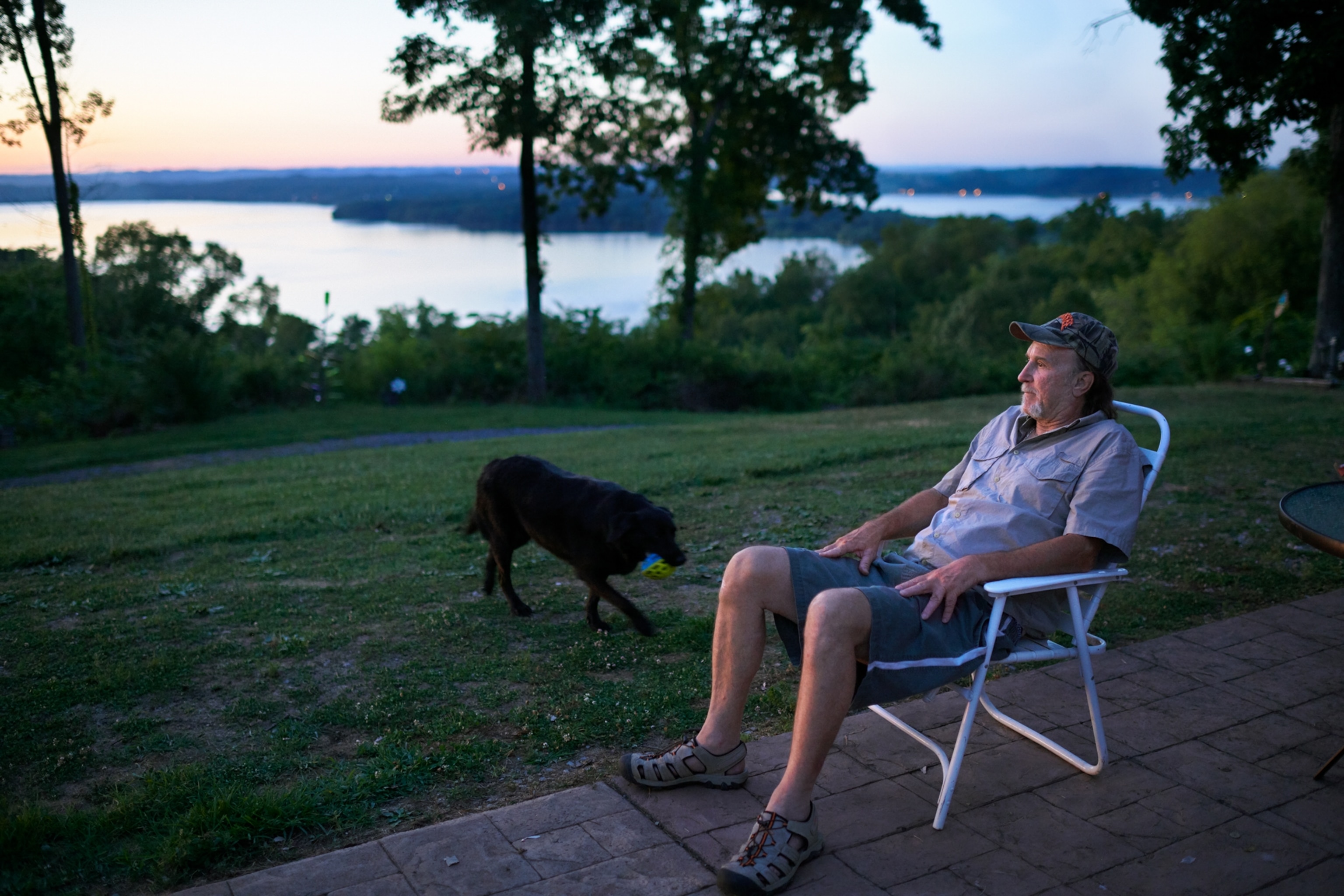 man sitting outdoor at waterfront and large black dog near him.
