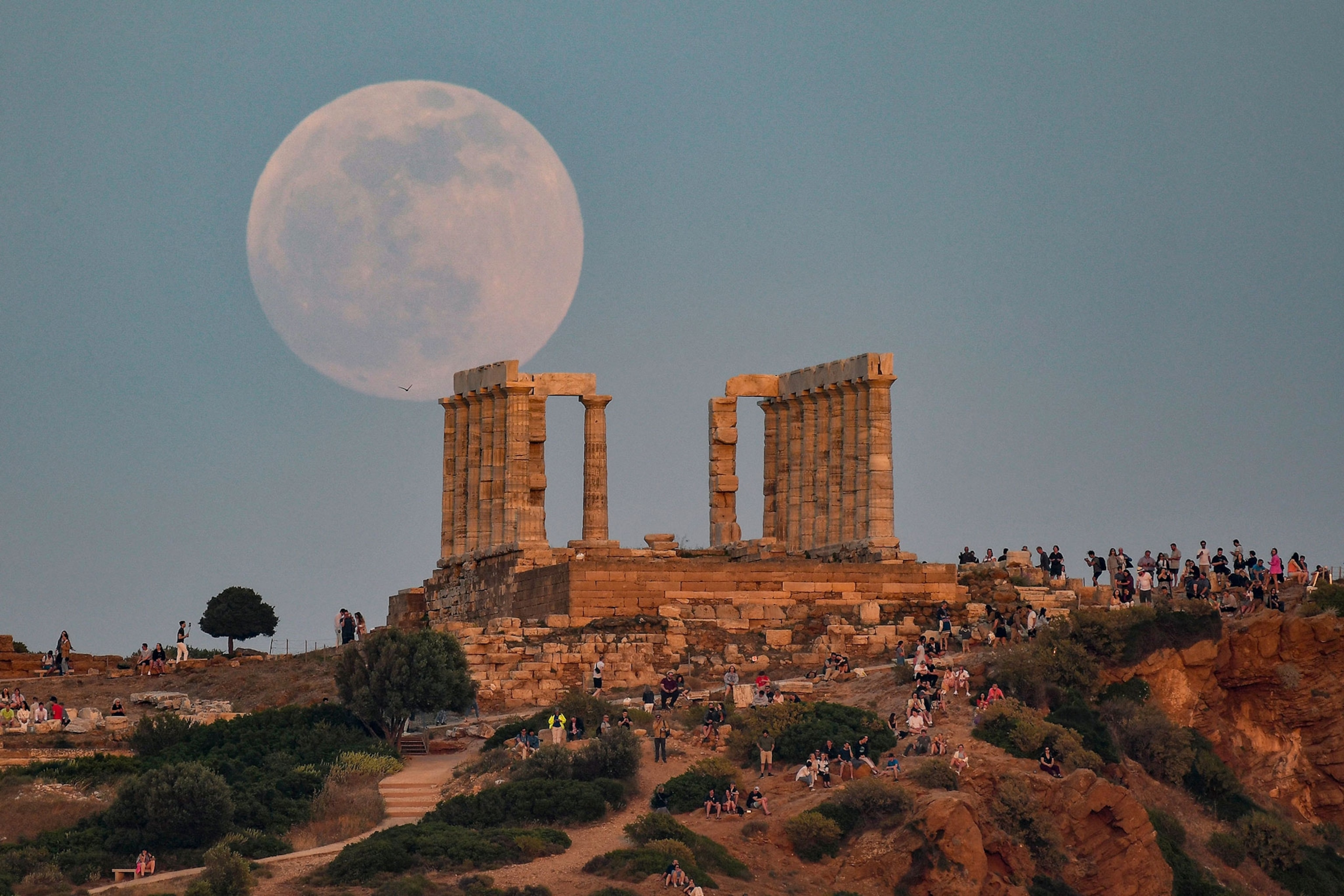 Greek ruins on a hill, at sunrise, with a gigantic, full moon close to the horizon