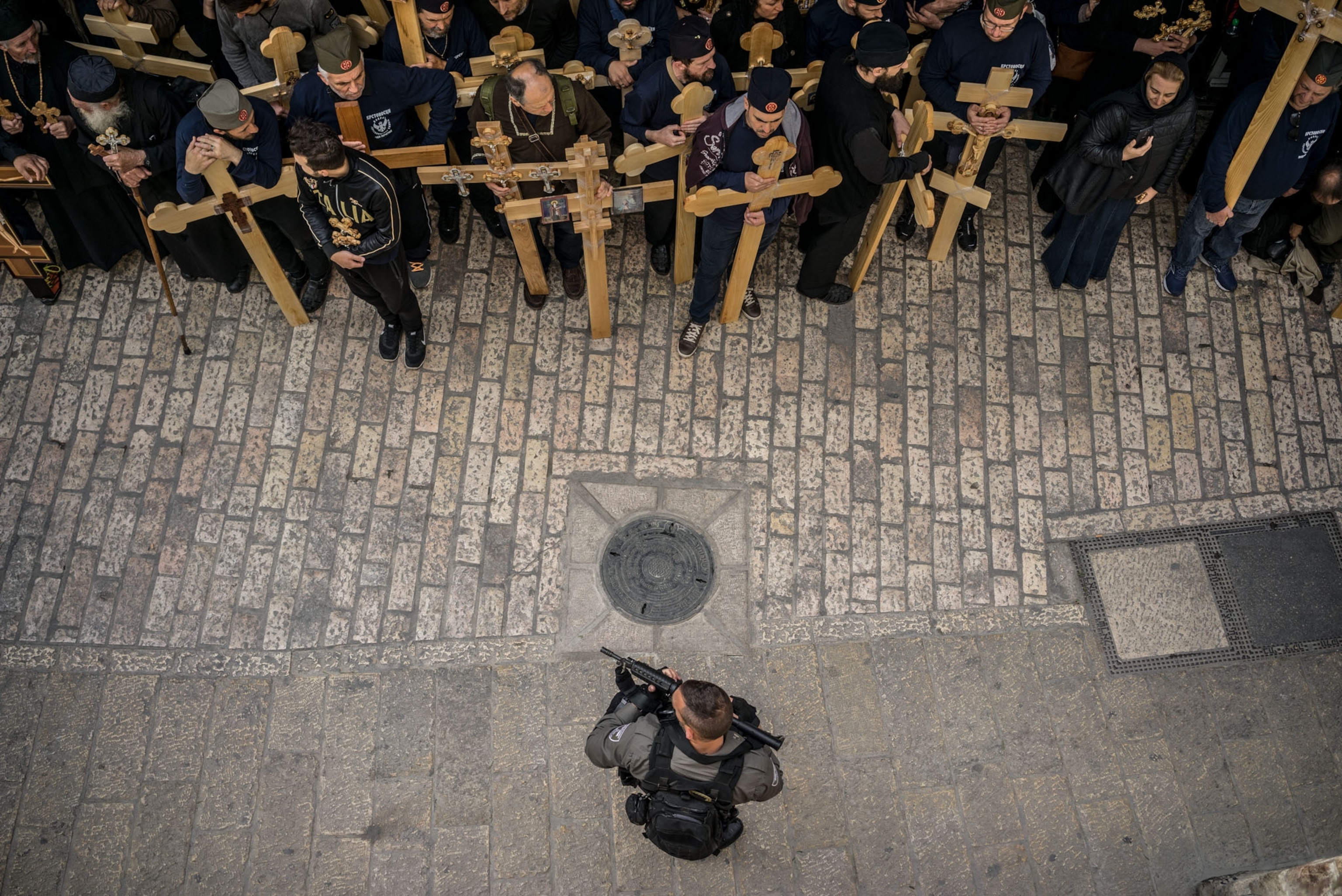 pilgrims with crosses and security office with automatic gun on cobblestone street.