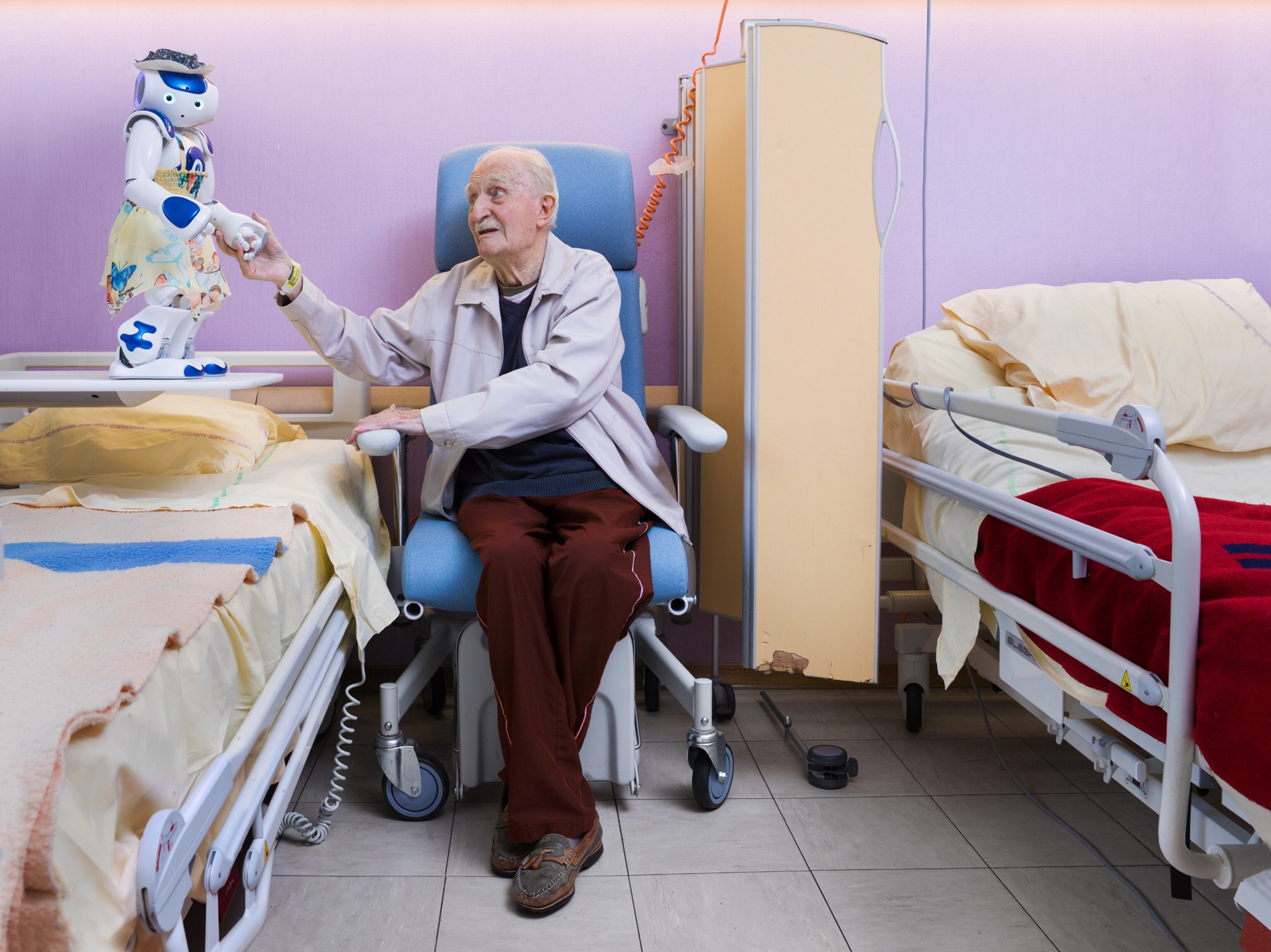 elderly man sitting in chair and holding robot's hand