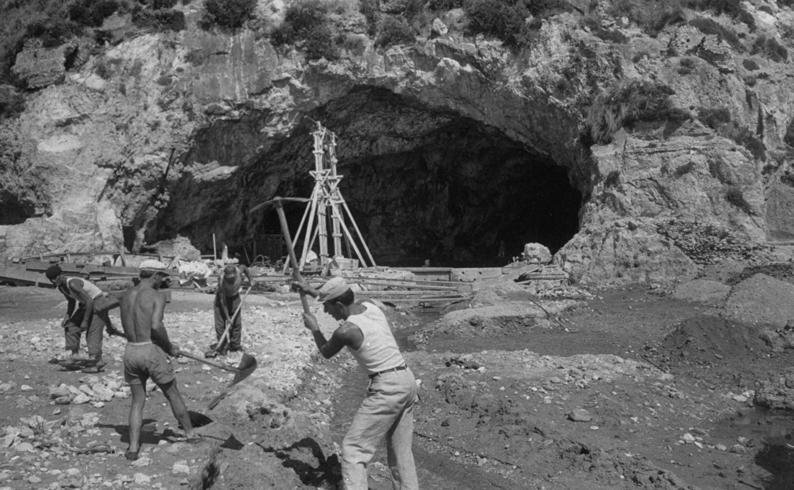 a black and white photo of men excavating near a cave in Italy