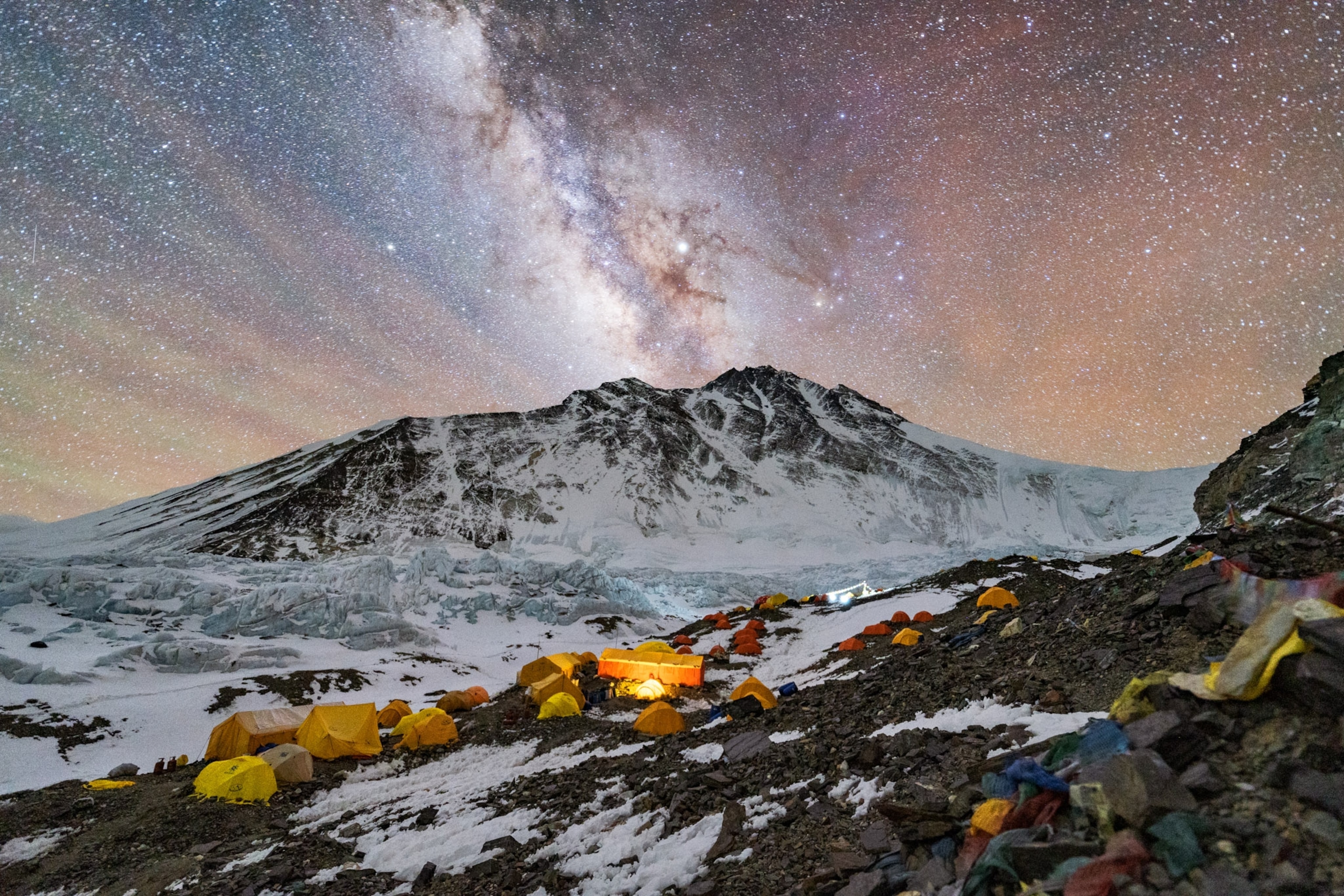 a row of yellow tents on a mountainside underneath the milkyway
