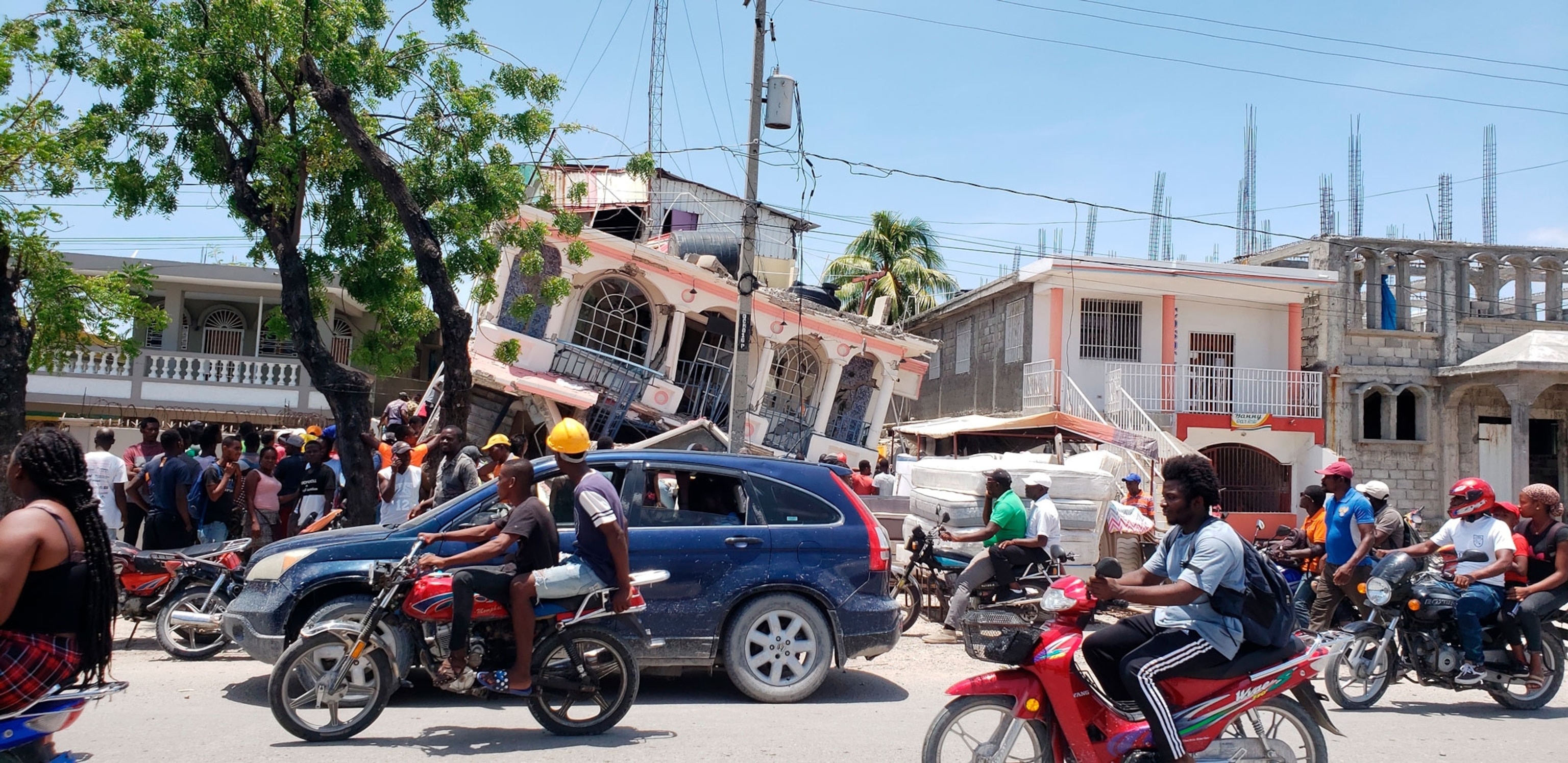 Busy traffic in the street moves past a hotel that partially crumbled in a recent earthquake.