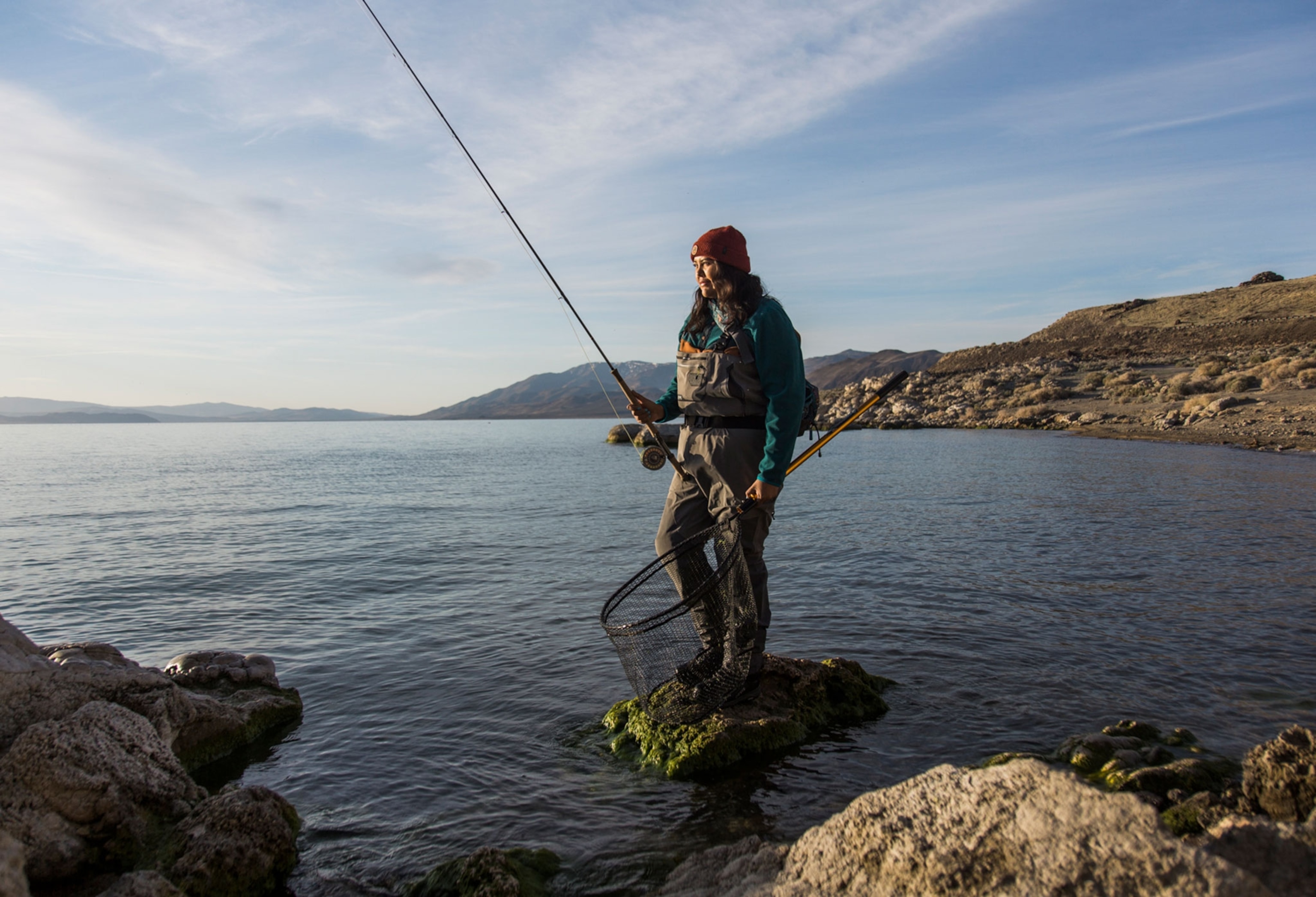 A woman standing on the edge of a lake fishing.