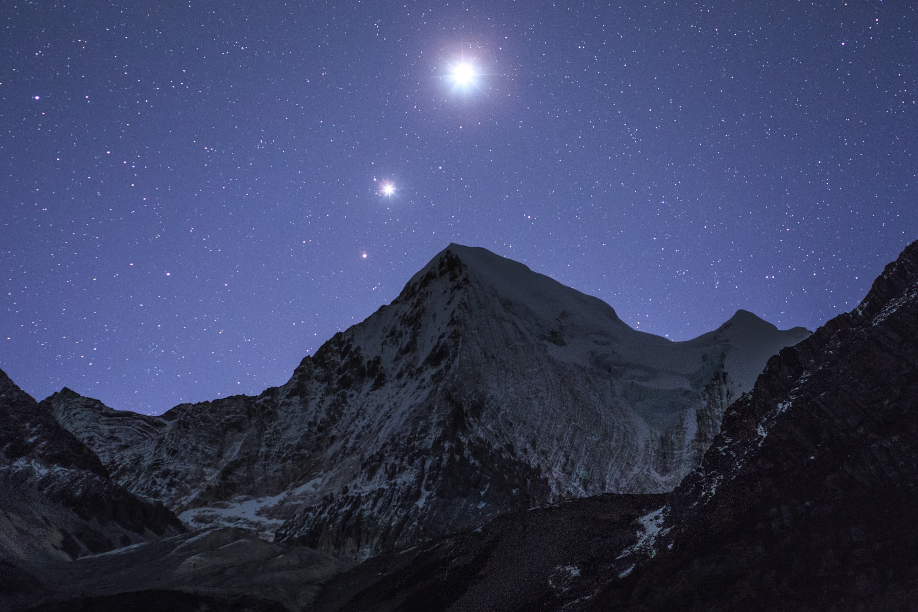 Three planets glowing brightly in the night sky over a mountain range.