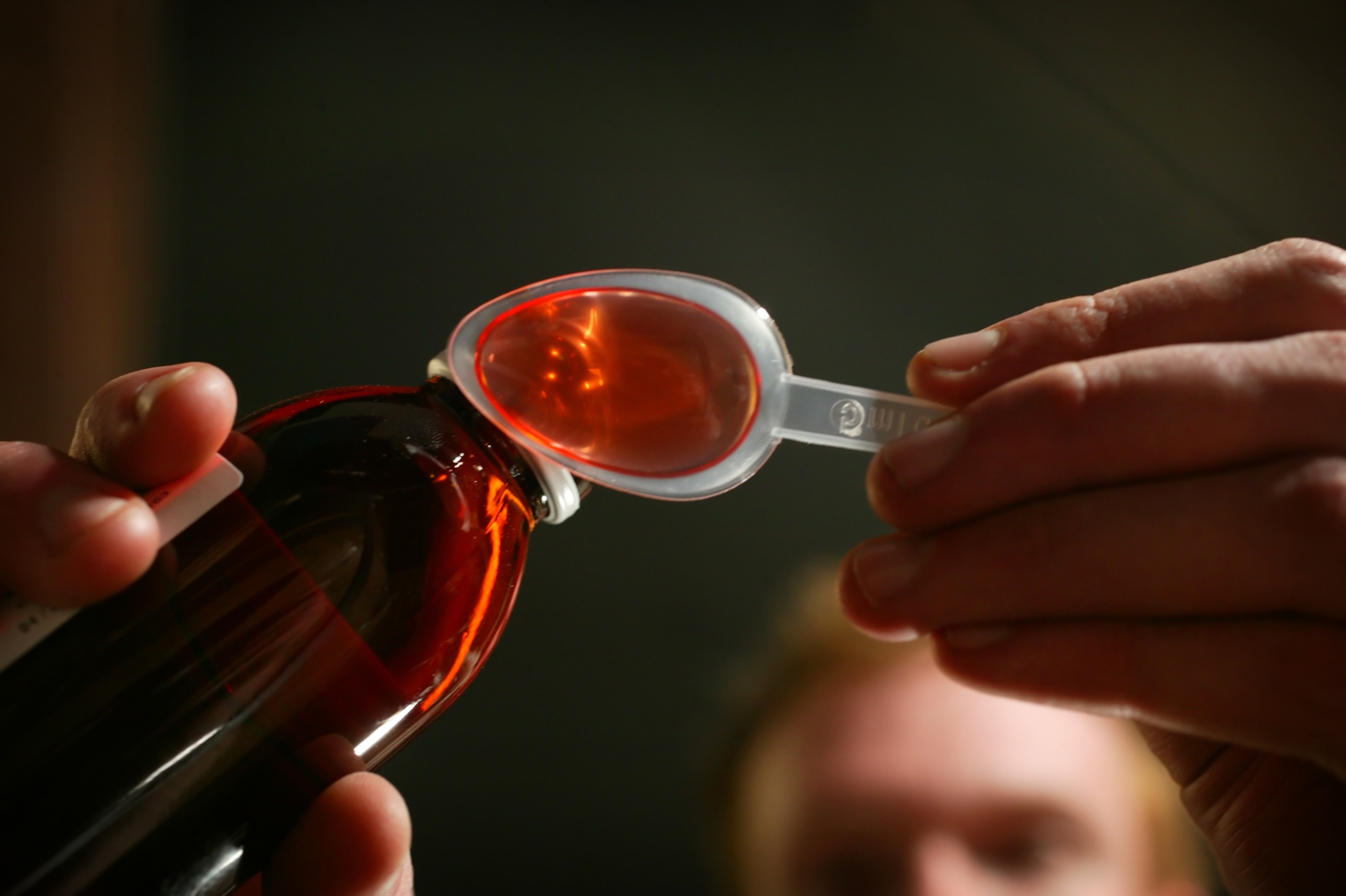 Red liquid medicine being poured into a clear spoon, seen from below