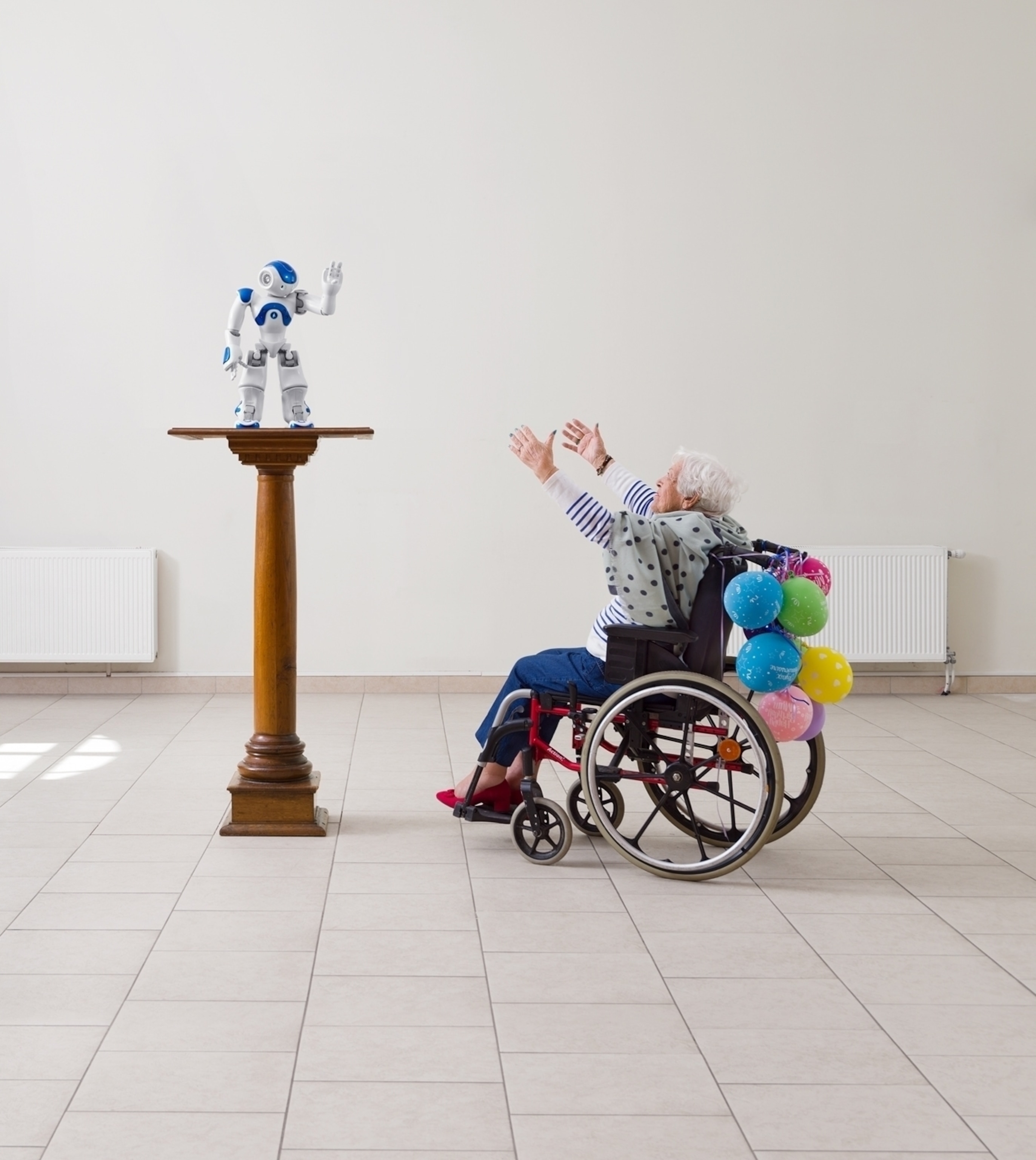 woman in wheelchair with hands stretched toward robot on pedestal.
