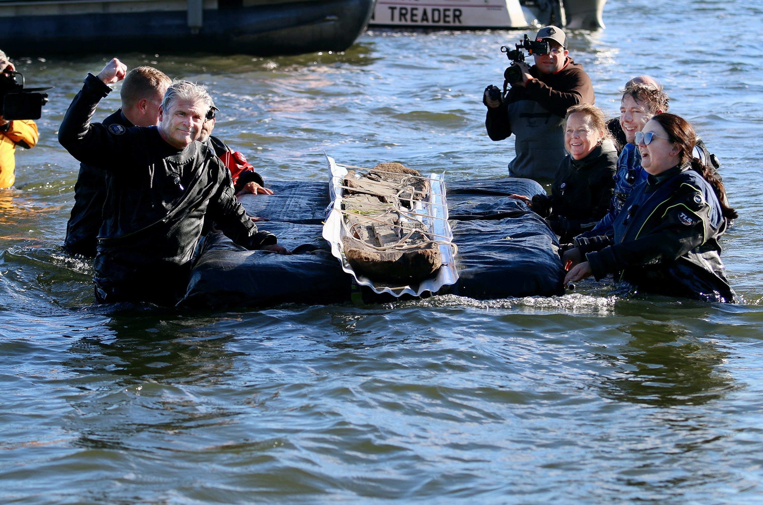 A group of people transition fragments of an artifact on a float together from the watter.